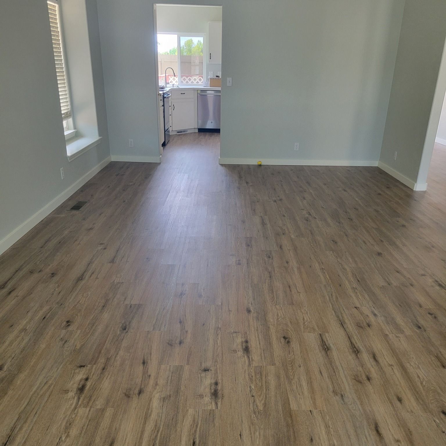 Empty room with wood-look flooring, white walls, and an open doorway to a kitchen area.