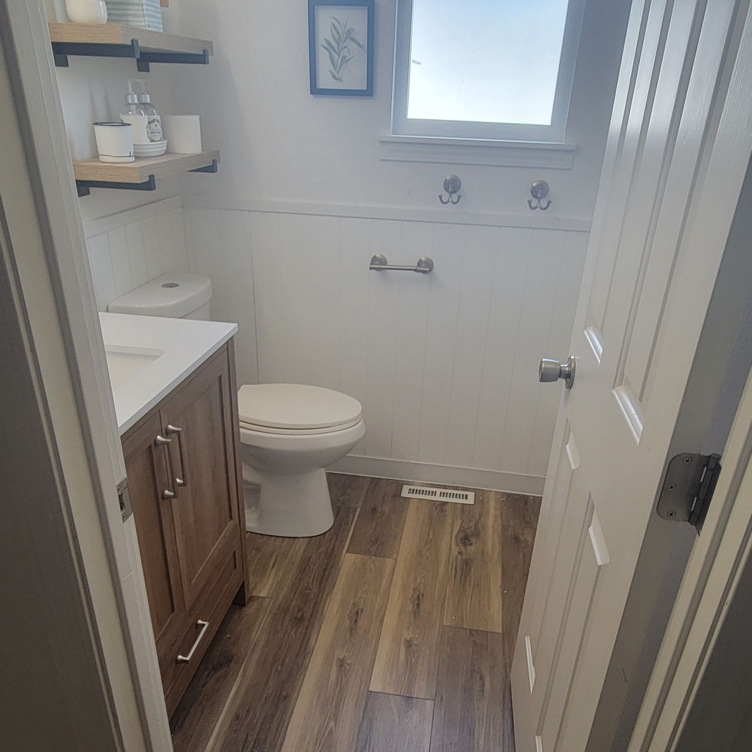 Bathroom with wood-look flooring, white walls, a toilet, vanity, and a partially open door.