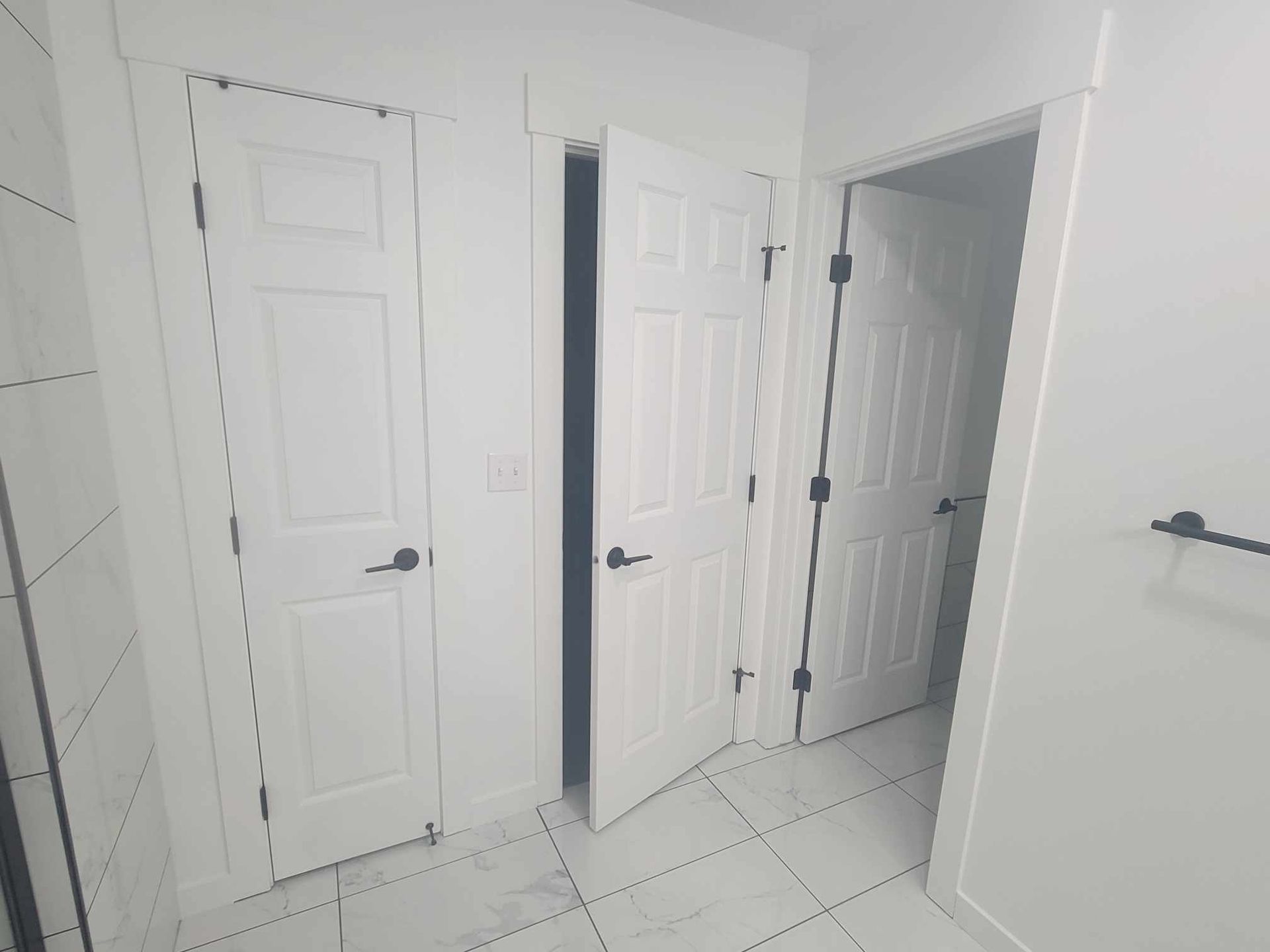 Three white interior doors, two closed and one open, in a bathroom. Black hardware on doors.