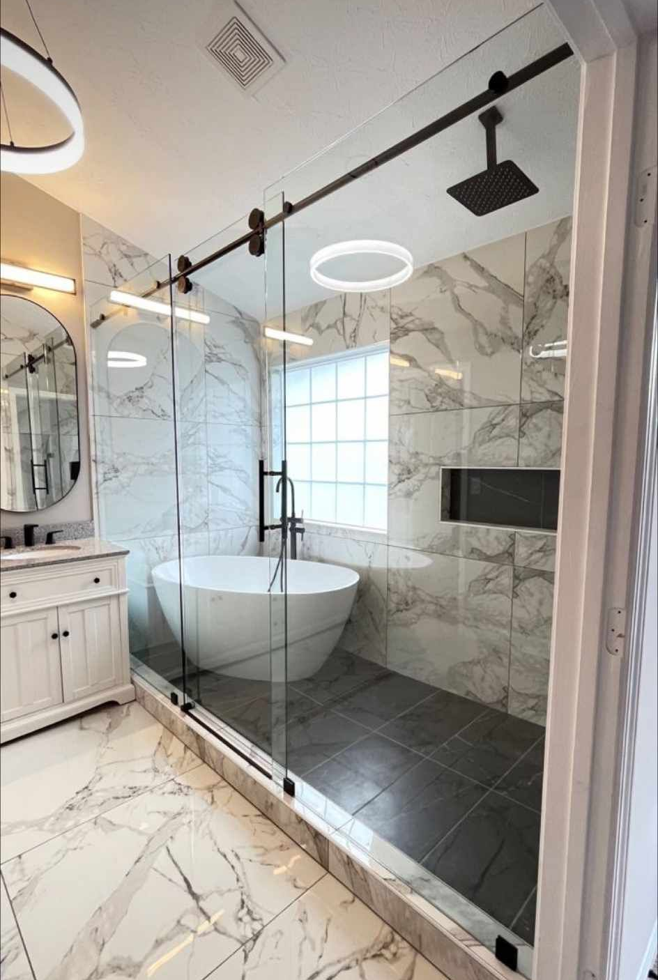Modern bathroom with a glass shower, white marble tile, and a soaking tub.