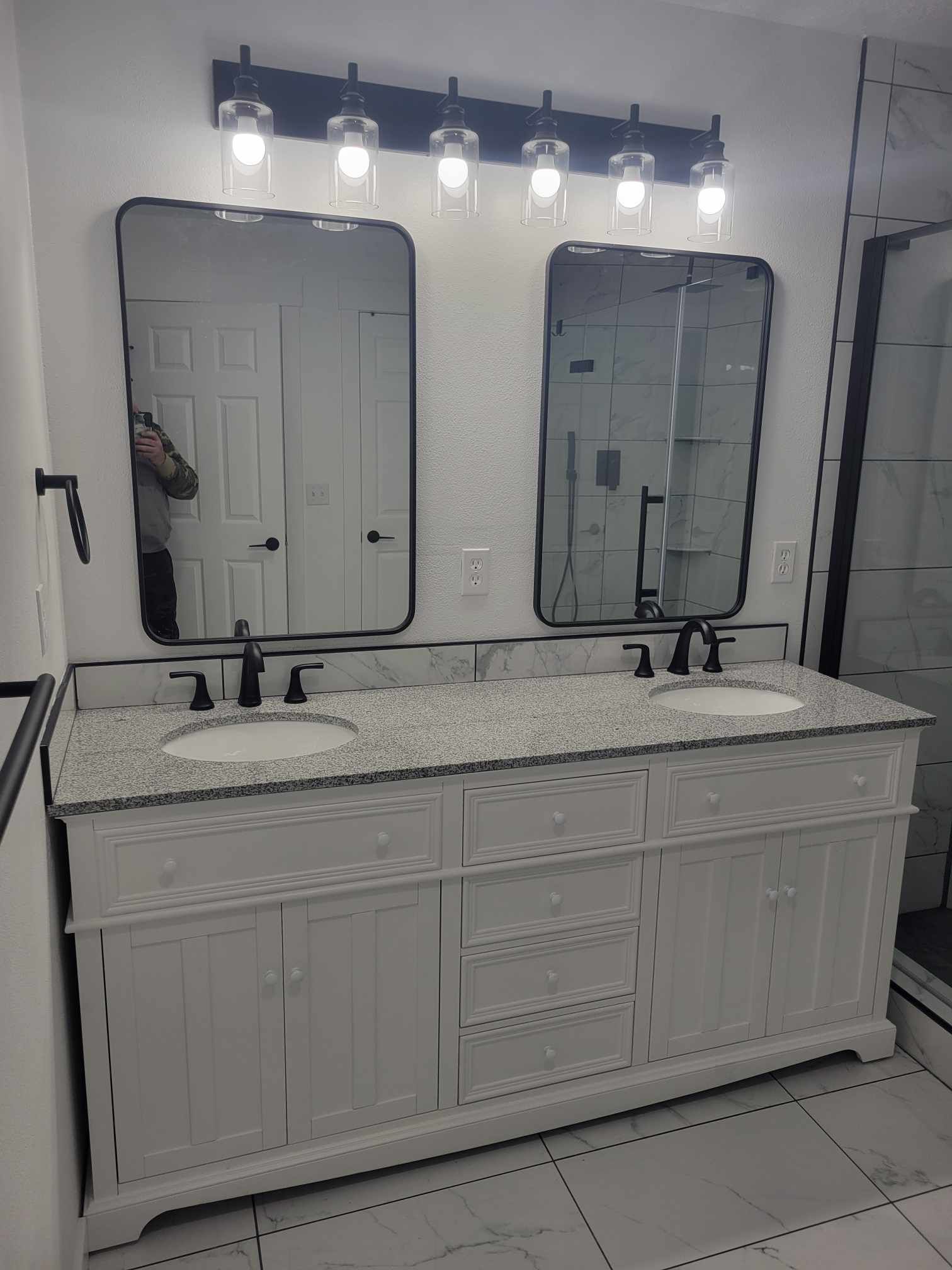 White double sink vanity with black mirrors and light fixture in a bathroom.