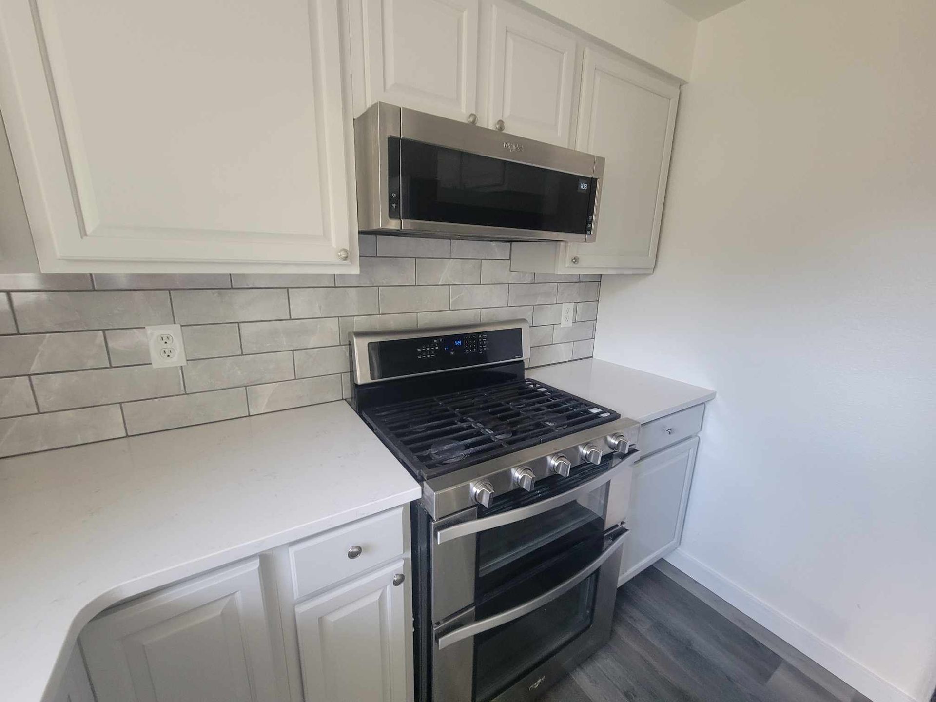 White kitchen with stainless steel appliances: oven, microwave, and stovetop with white cabinets and backsplash.