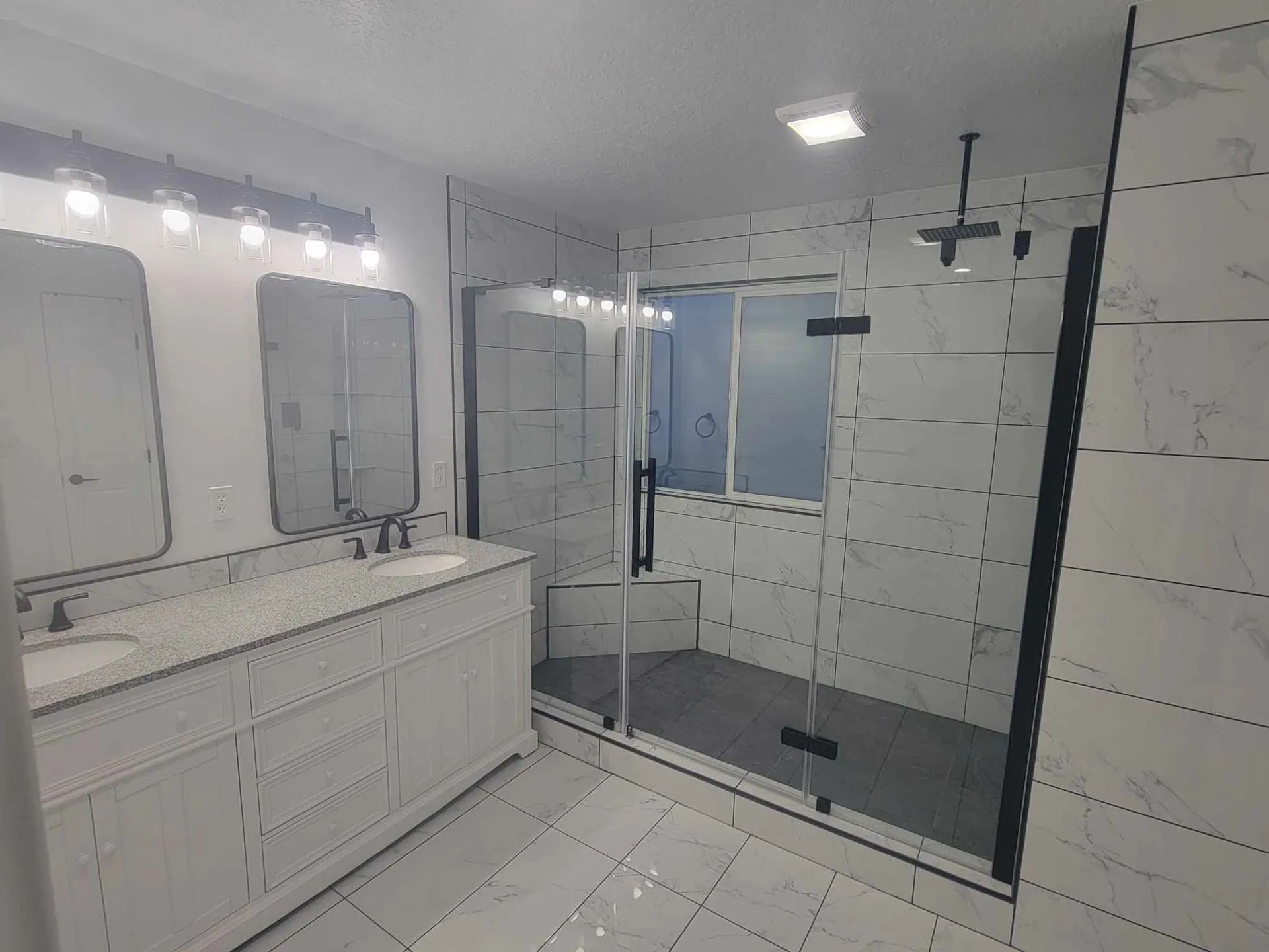 Bathroom with white marble tile, double vanity, and glass shower enclosure.