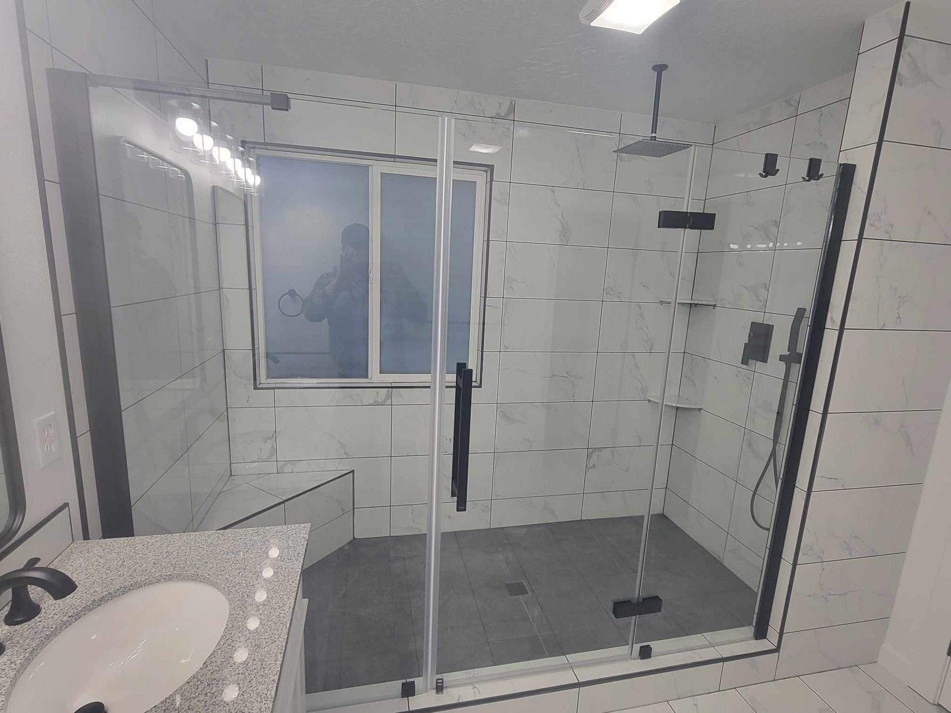 Modern bathroom with gray floor, white tiles, glass shower, and black fixtures.