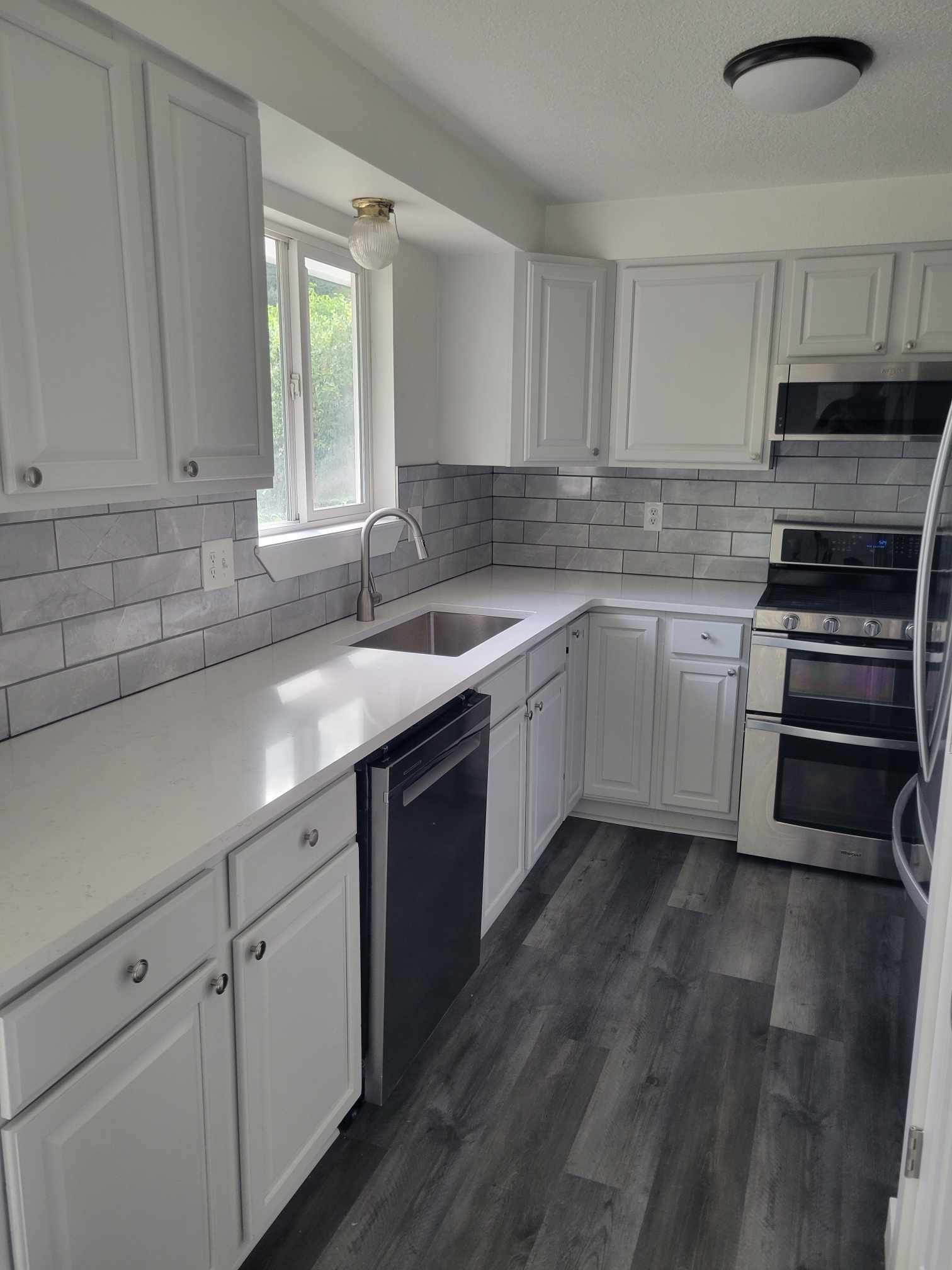 White kitchen with gray countertops, stainless steel appliances, and gray tile backsplash.