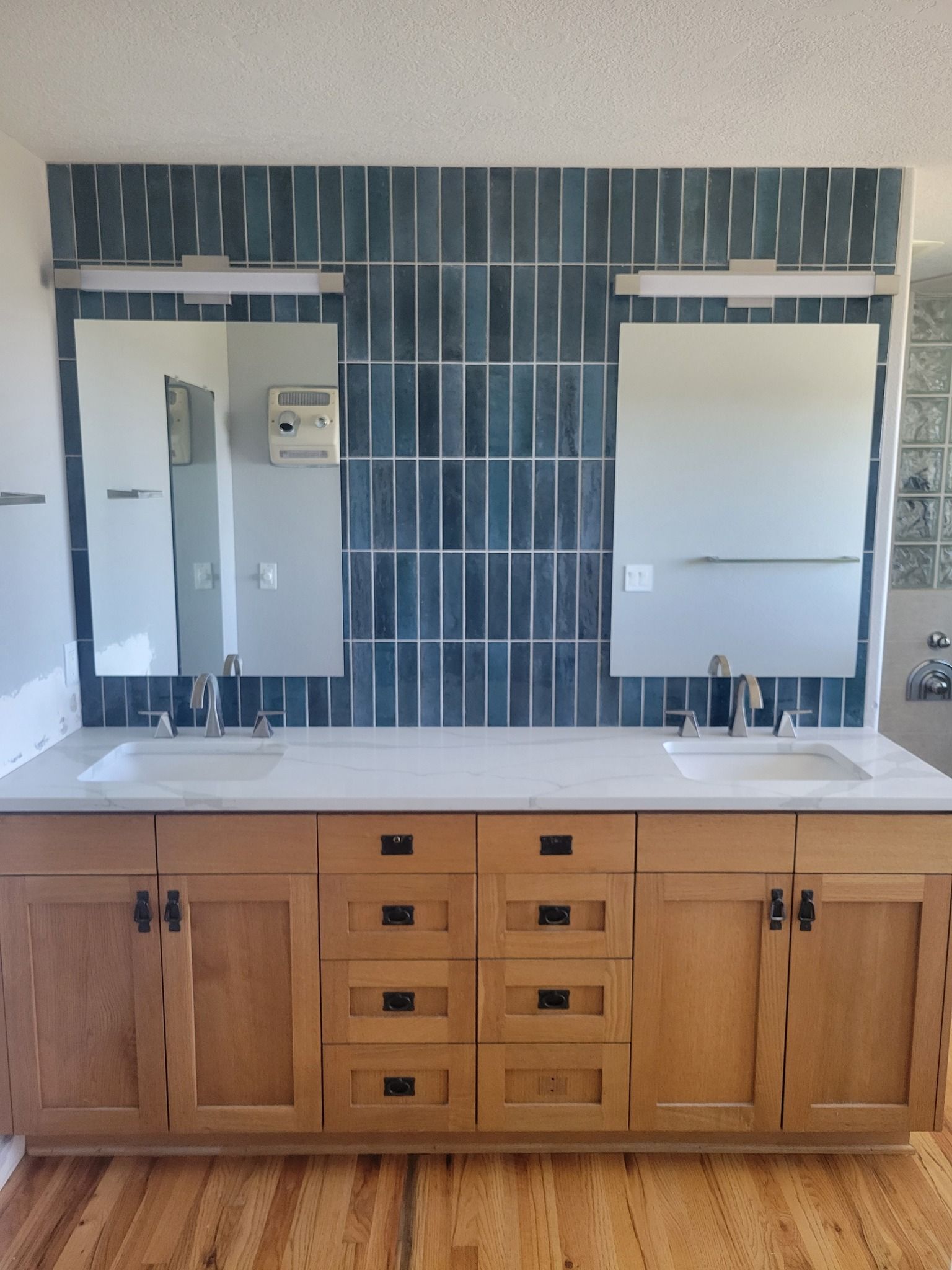 Bathroom vanity with two sinks, mirrors, blue tile backsplash, and wood cabinets.