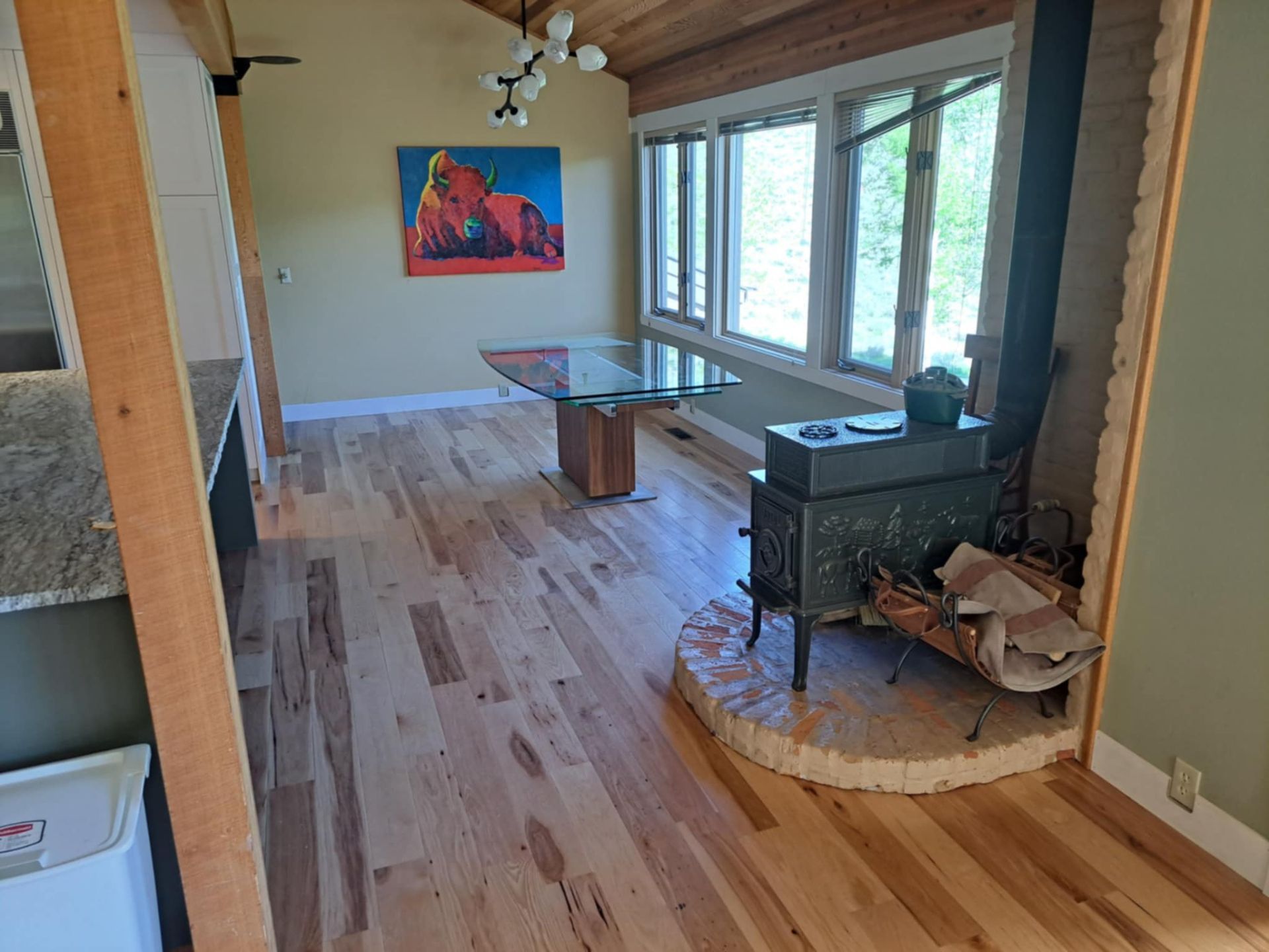 A light-filled room with wood floors, a dining table, windows, and a wood-burning stove.