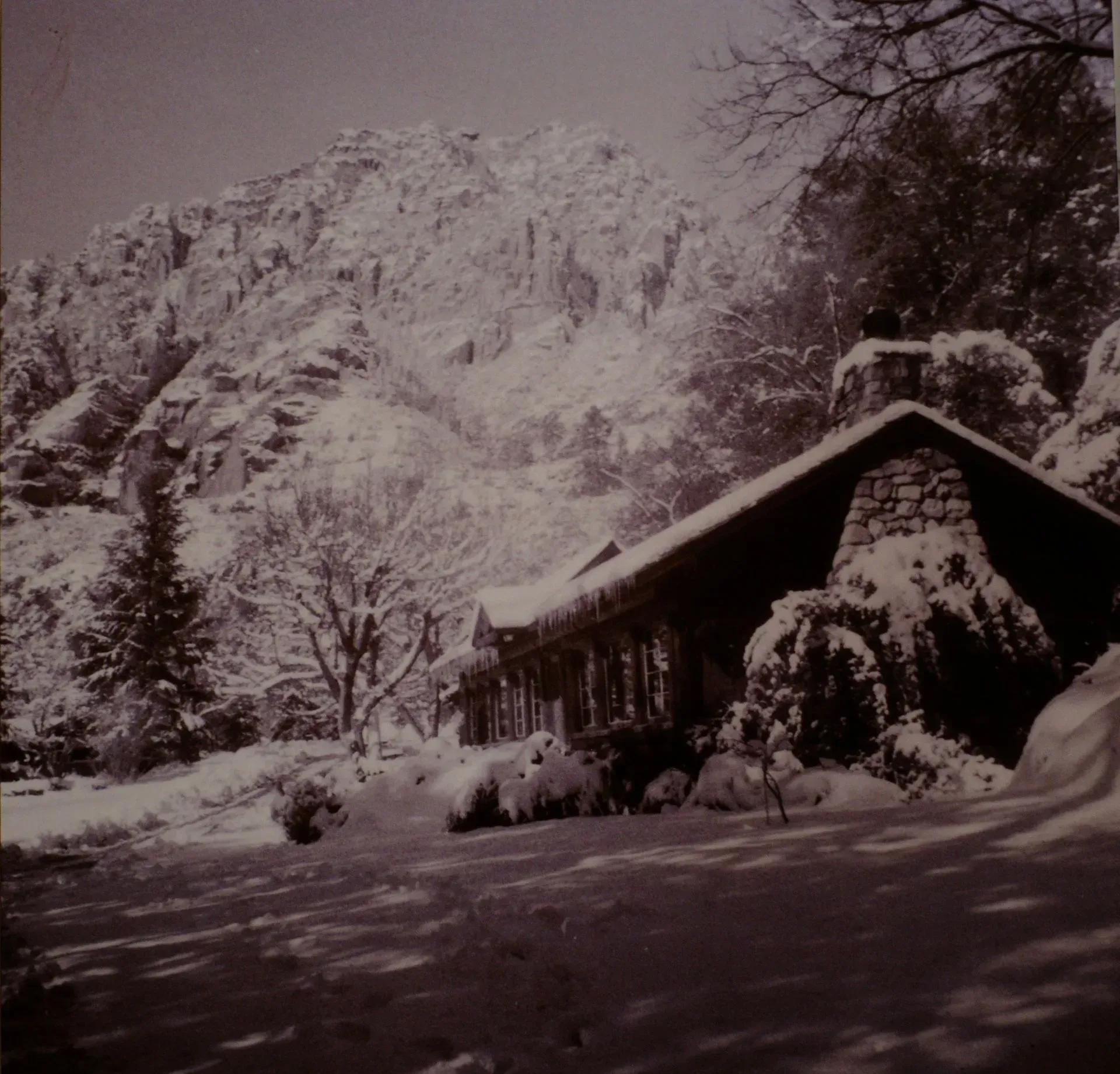 Snow-covered cabin nestled in a snowy mountain landscape, with trees and a snow-covered roof.