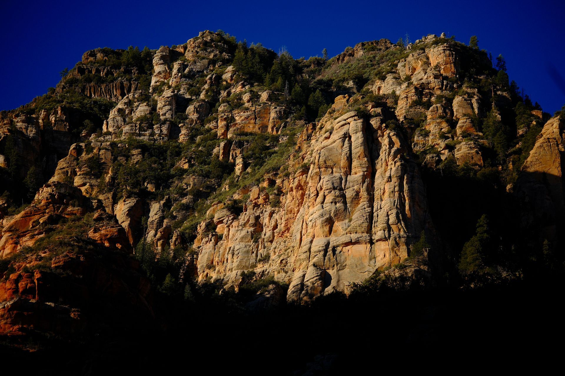 Rocky mountain peak, lit by sunlight. Dark blue sky.