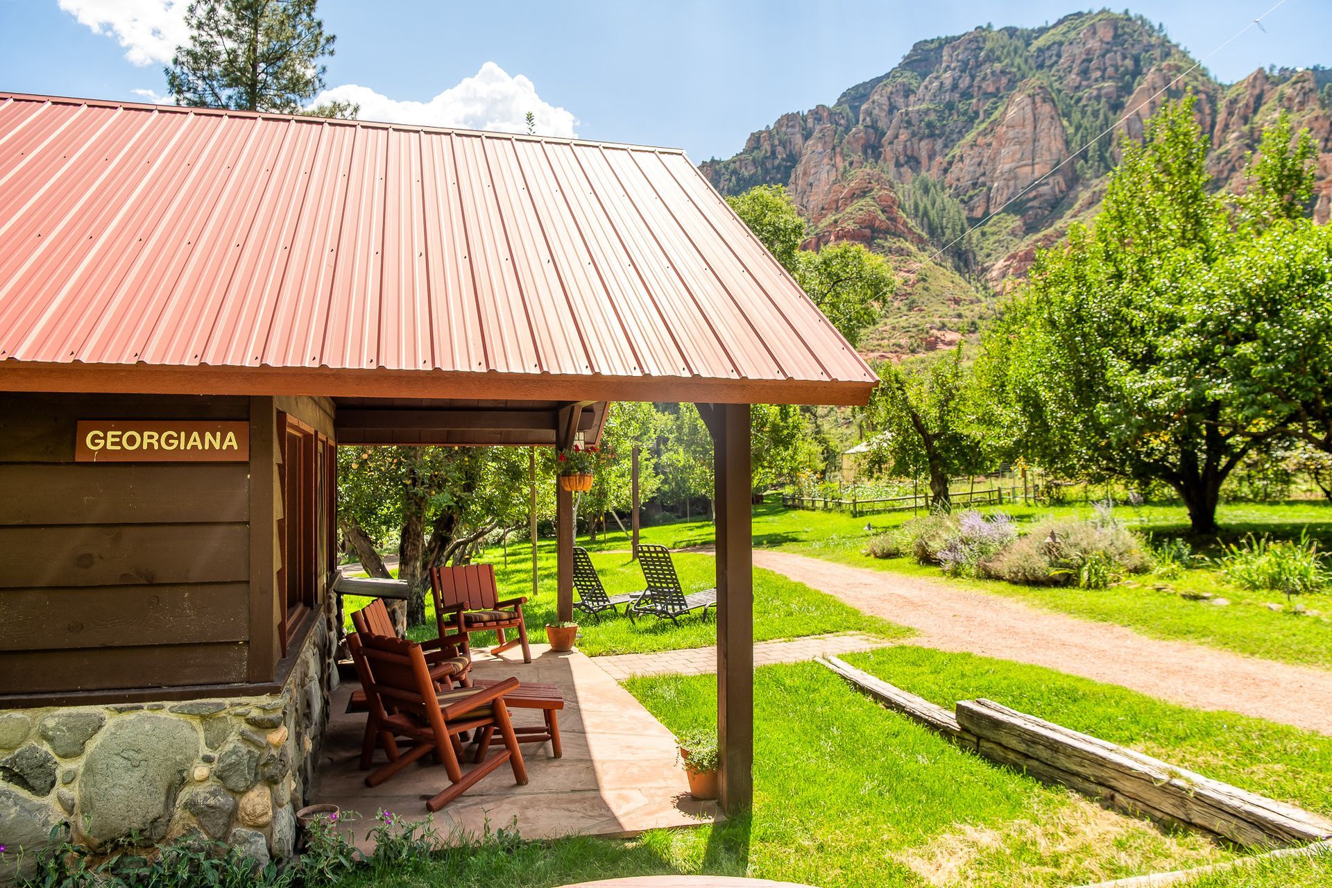 Cabin with red roof and porch, chairs on porch, mountains in background.