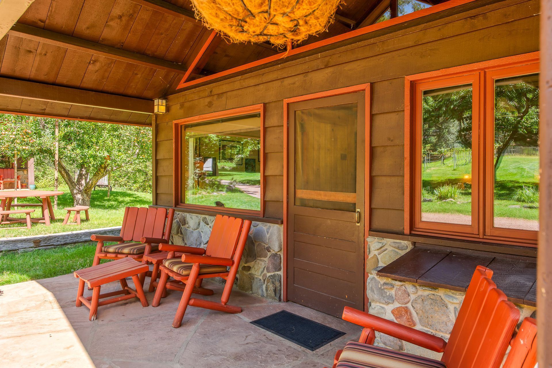 Covered porch with orange chairs, screen door, and windows of a cabin with yard.