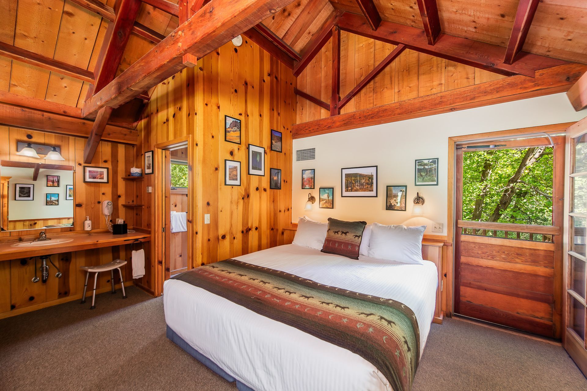 Cozy wooden cabin bedroom with a bed, vanity, and open door to greenery.