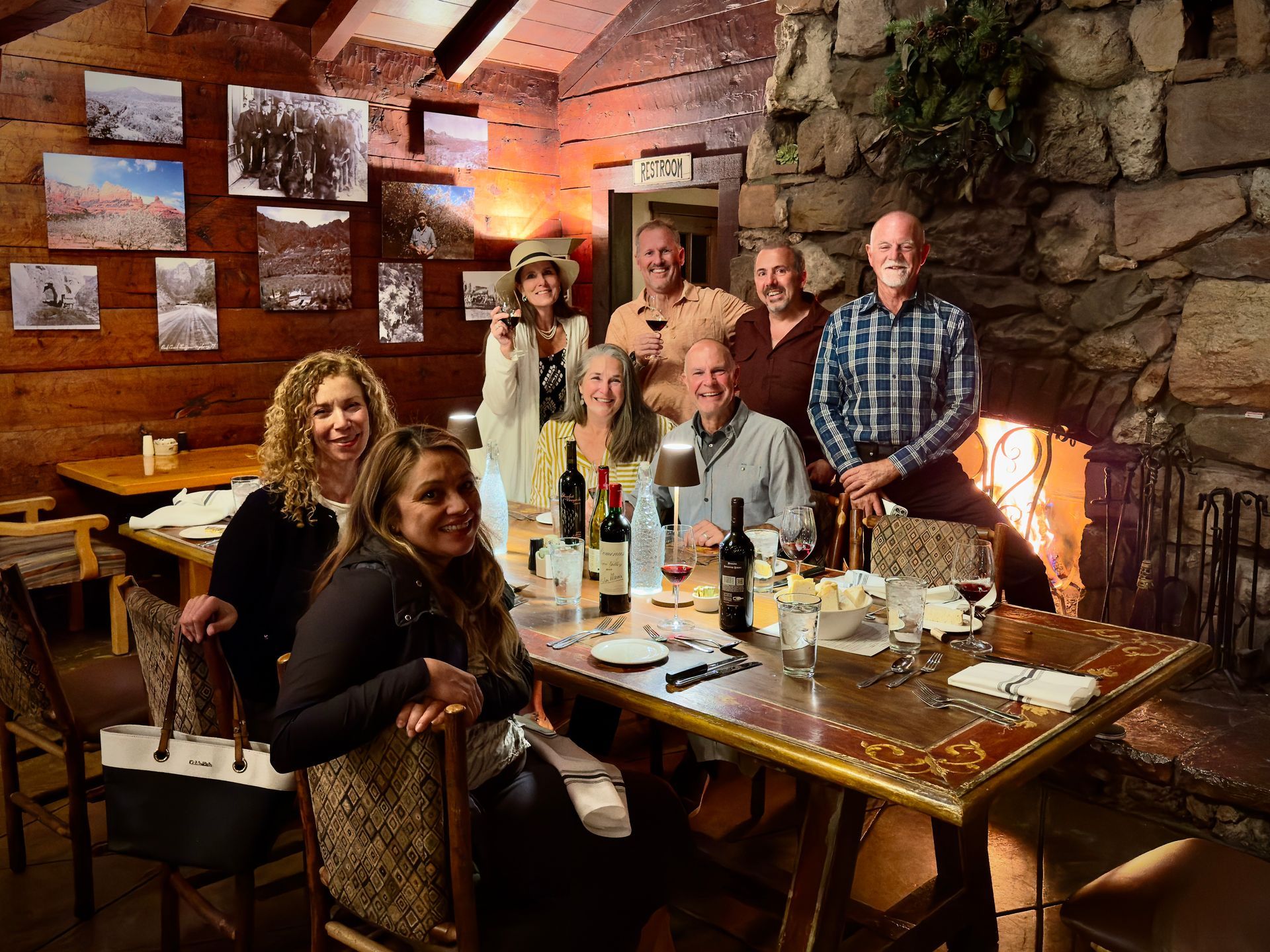 Group of people at a table in a cozy restaurant. Dark wood walls, fireplace, and art add warmth.