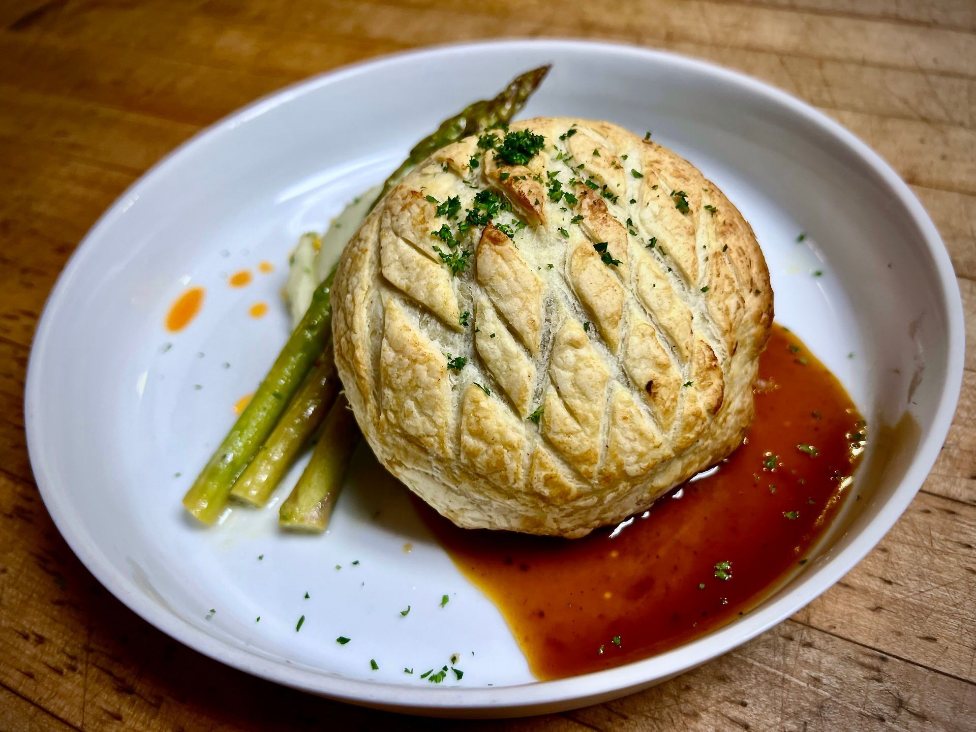 Beef Wellington with asparagus, sauce, and parsley on a white plate.