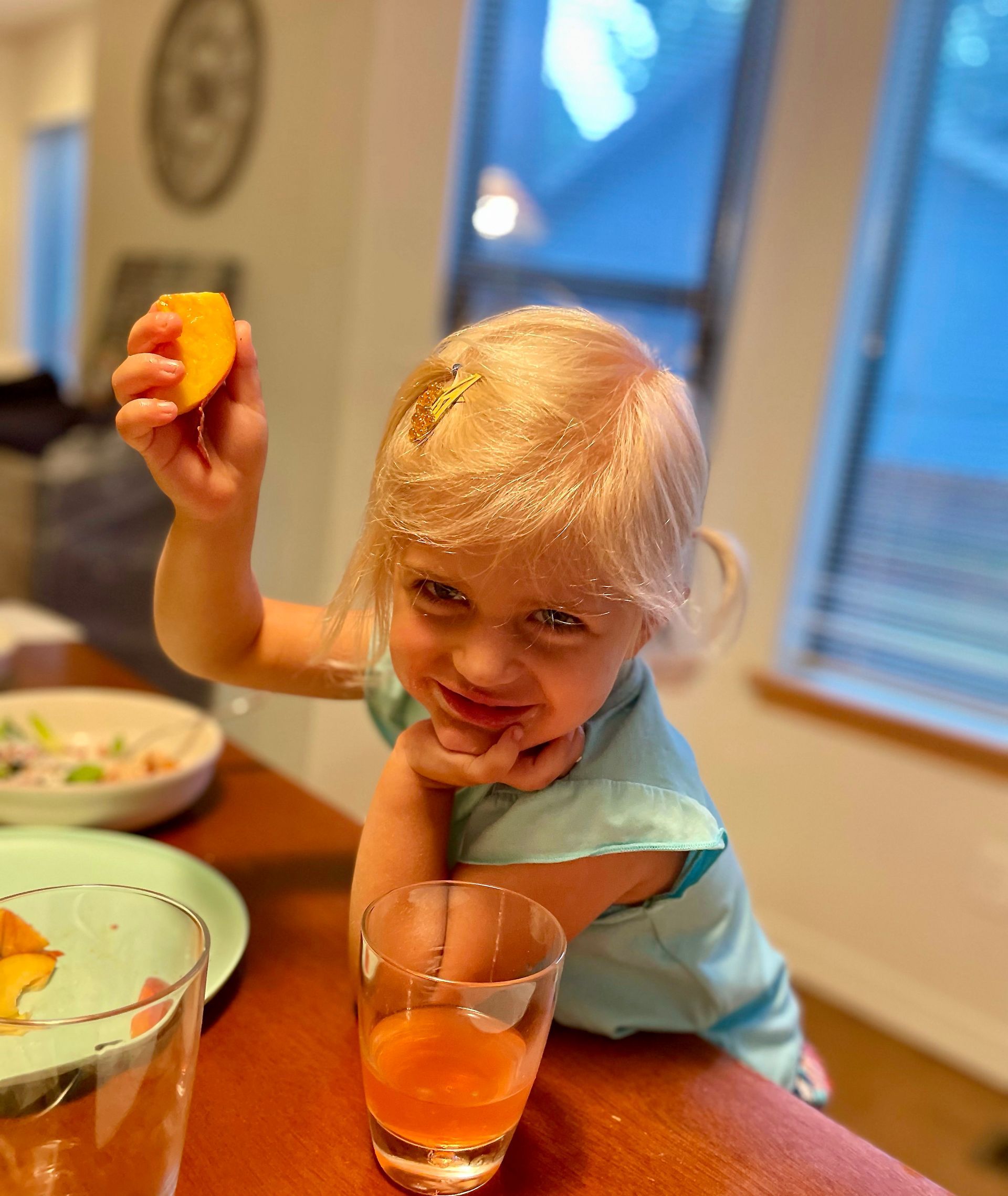 A young child with a slice of orange in their raised hand, covered in orange powder, standing near a drink.