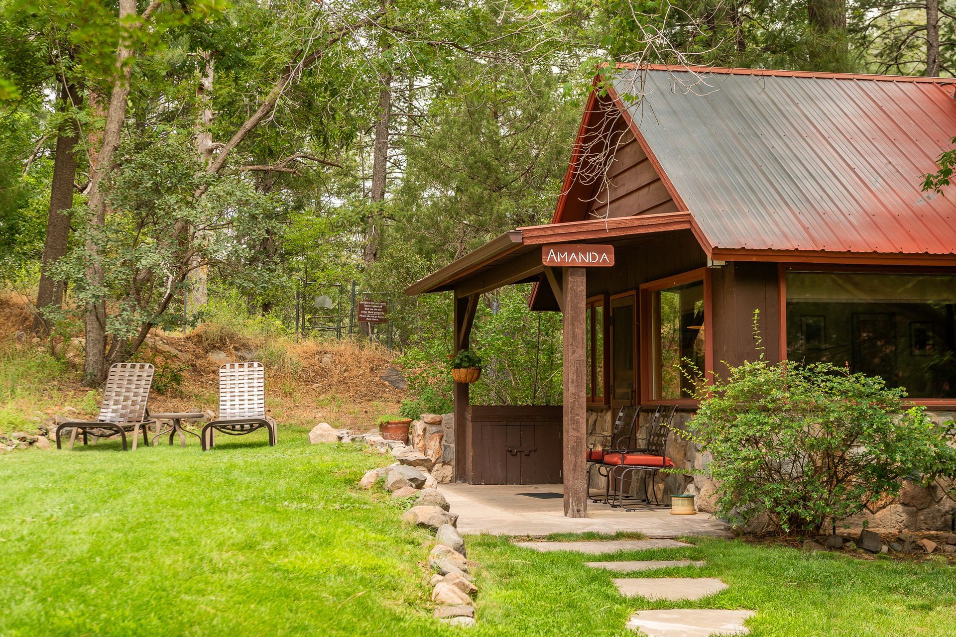 Rustic cabin with a red roof, porch, and lawn with lounge chairs.