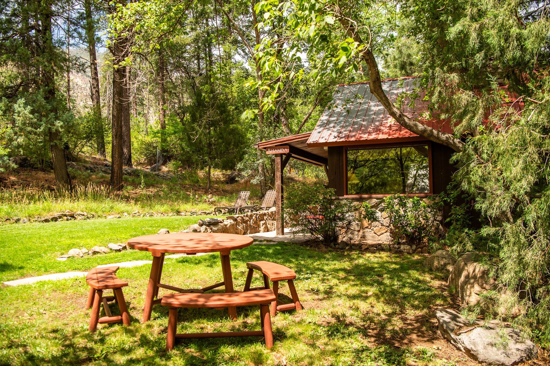 Wooden picnic table and benches in a sunny, green garden with a gazebo.