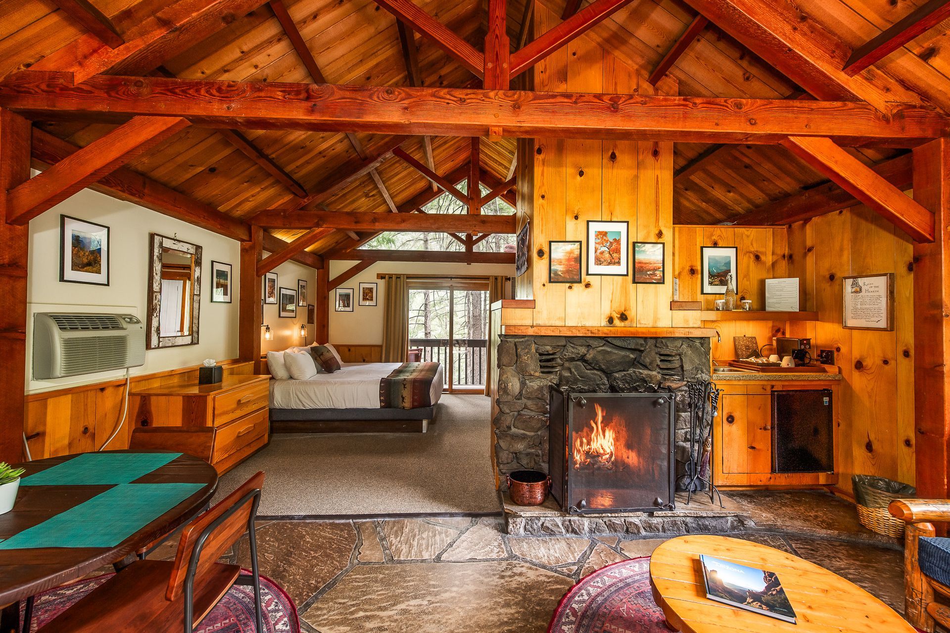 Cozy cabin interior with exposed wood beams, fireplace, and open view to a bed.