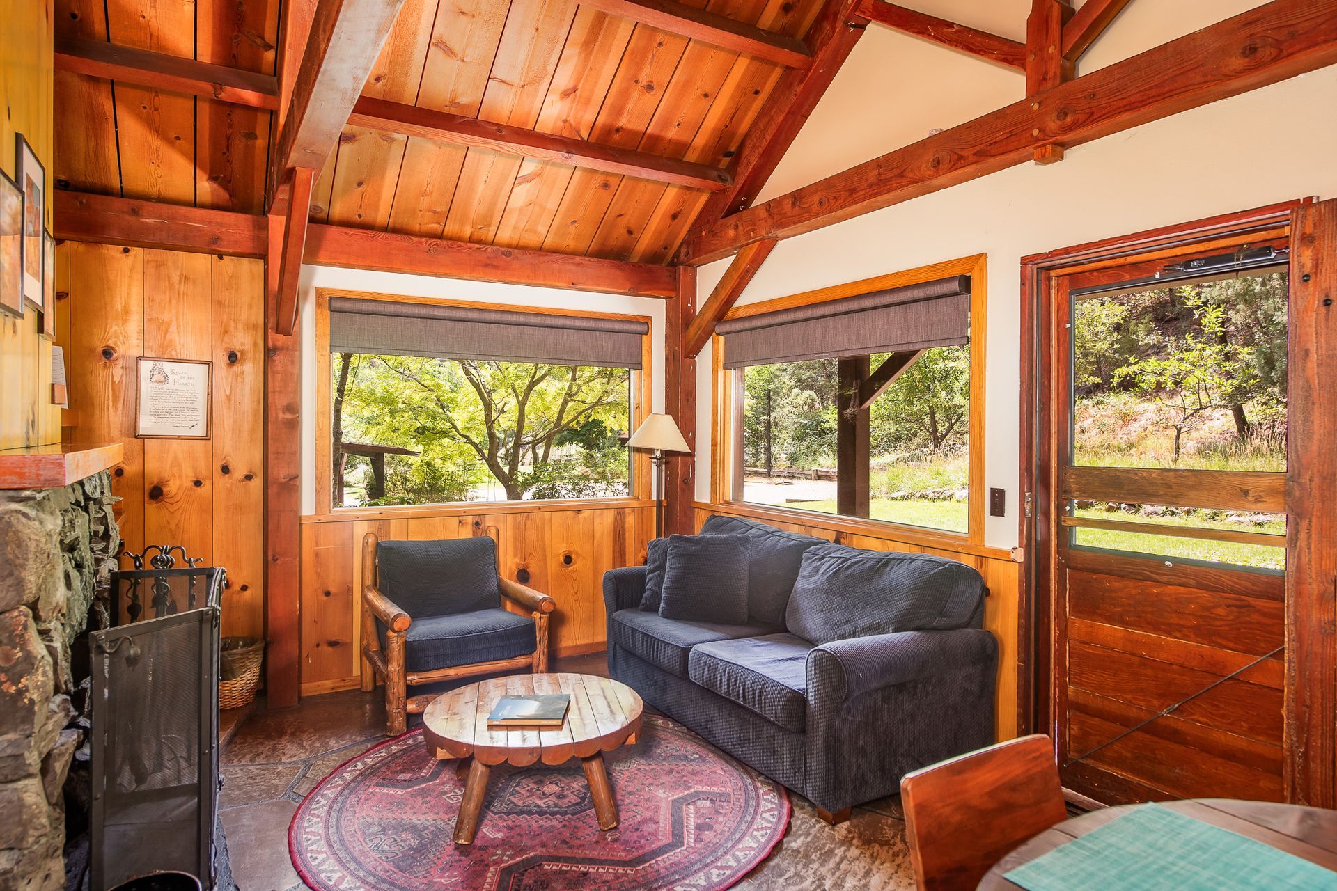 Cozy cabin interior with wooden walls and ceiling, sofa, chair, round table, and window with outdoor view.