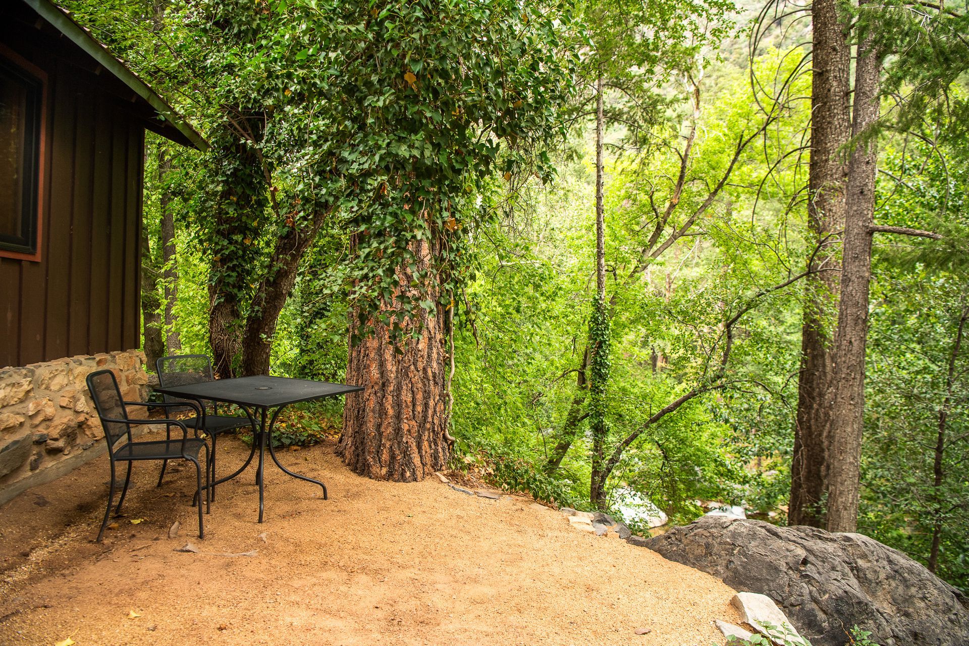 Cabin exterior with table and chairs, forest backdrop.