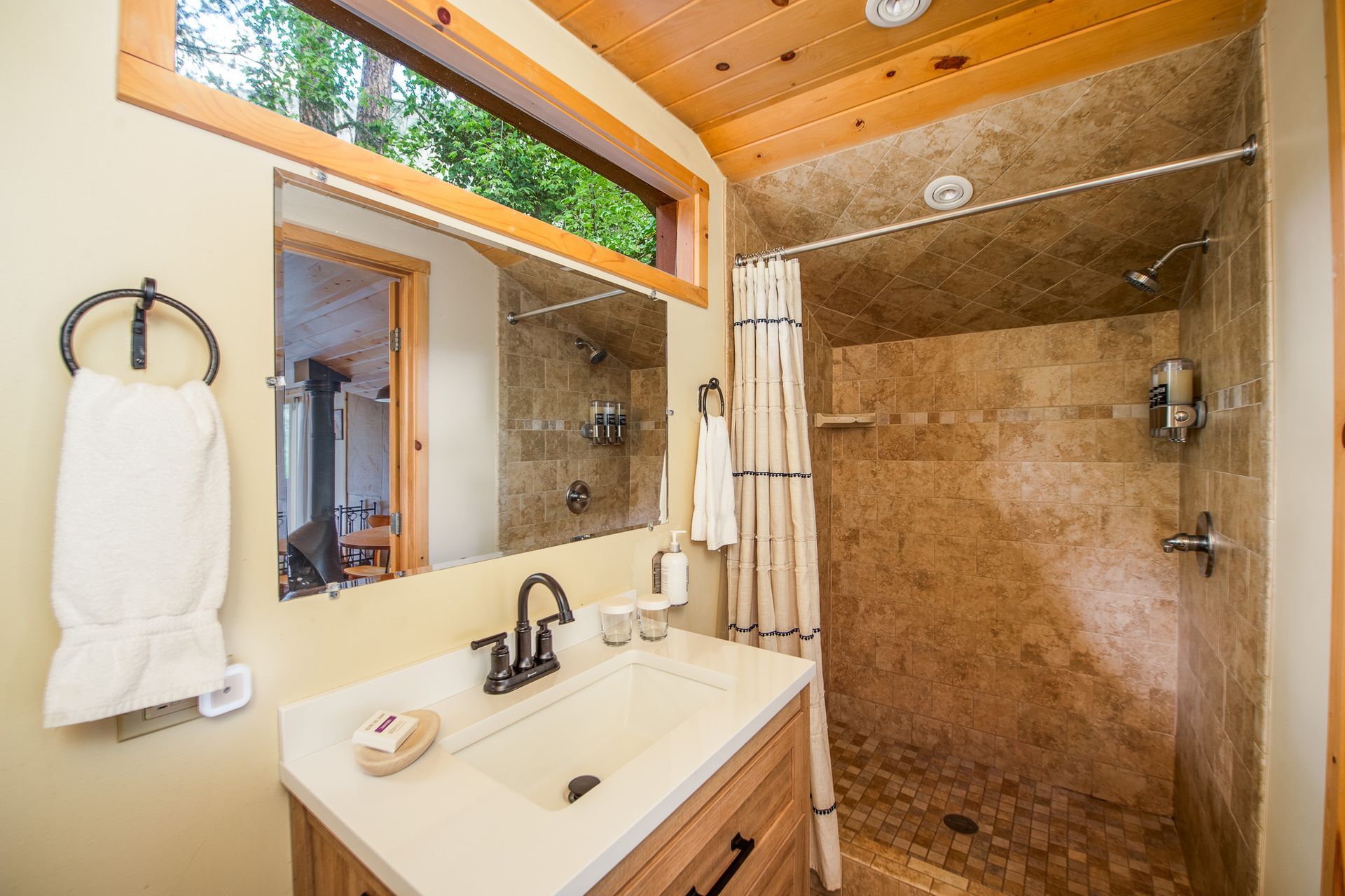 Bathroom with beige walls, stone shower, wooden vanity, large mirror, and towel.