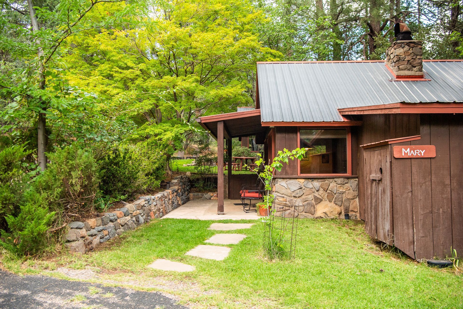 A small cabin with a stone facade and metal roof nestled in a wooded area.