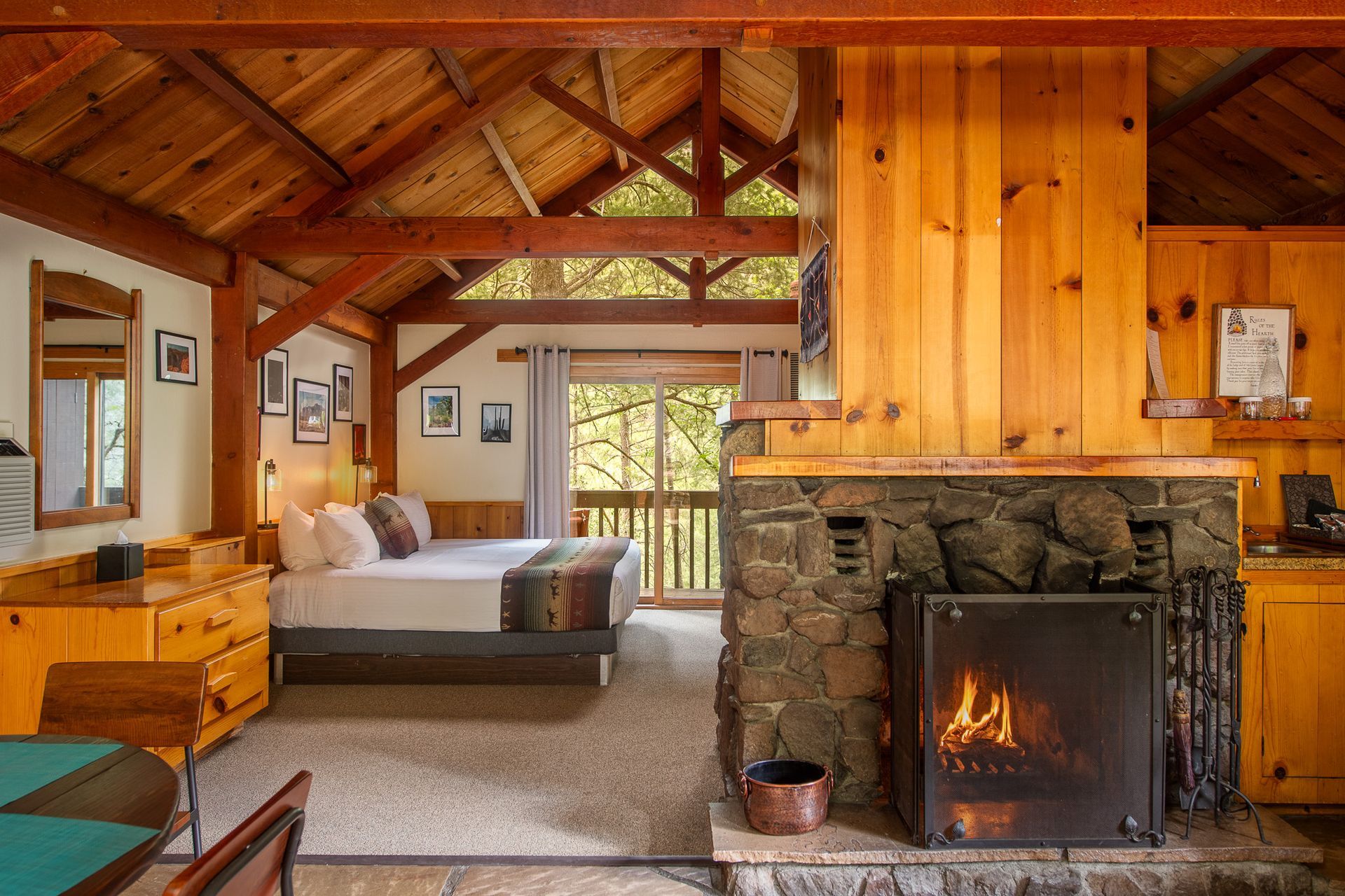 Rustic cabin interior with fireplace, bed, and balcony overlooking trees.