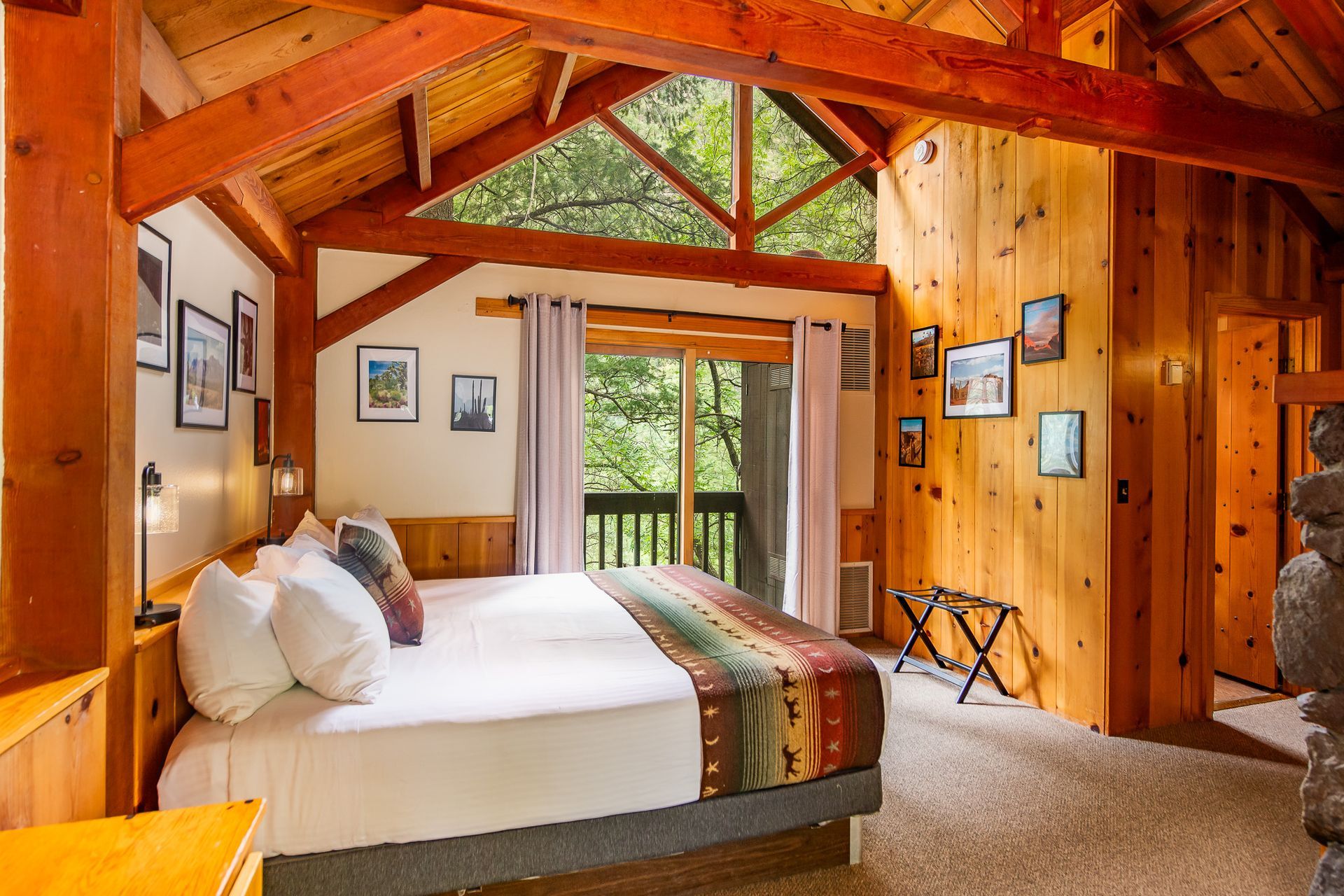 Bedroom with a large bed, wooden walls, and a balcony overlooking trees.