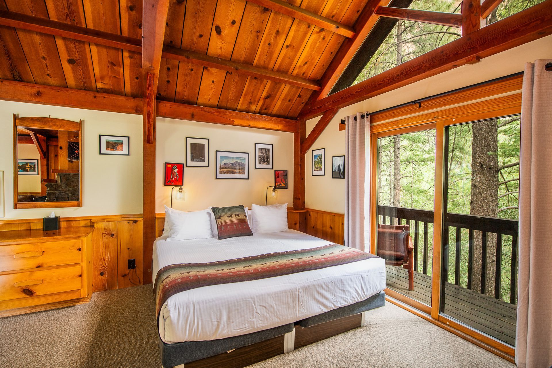 Bedroom with wood paneling, a queen bed, and a balcony overlooking a forest.