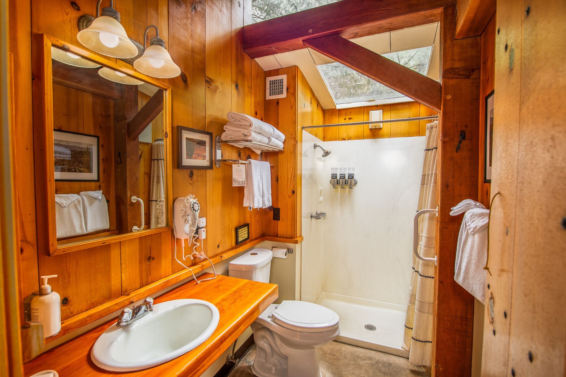 Bathroom with wood-paneled walls, a sink, toilet, shower, and window.