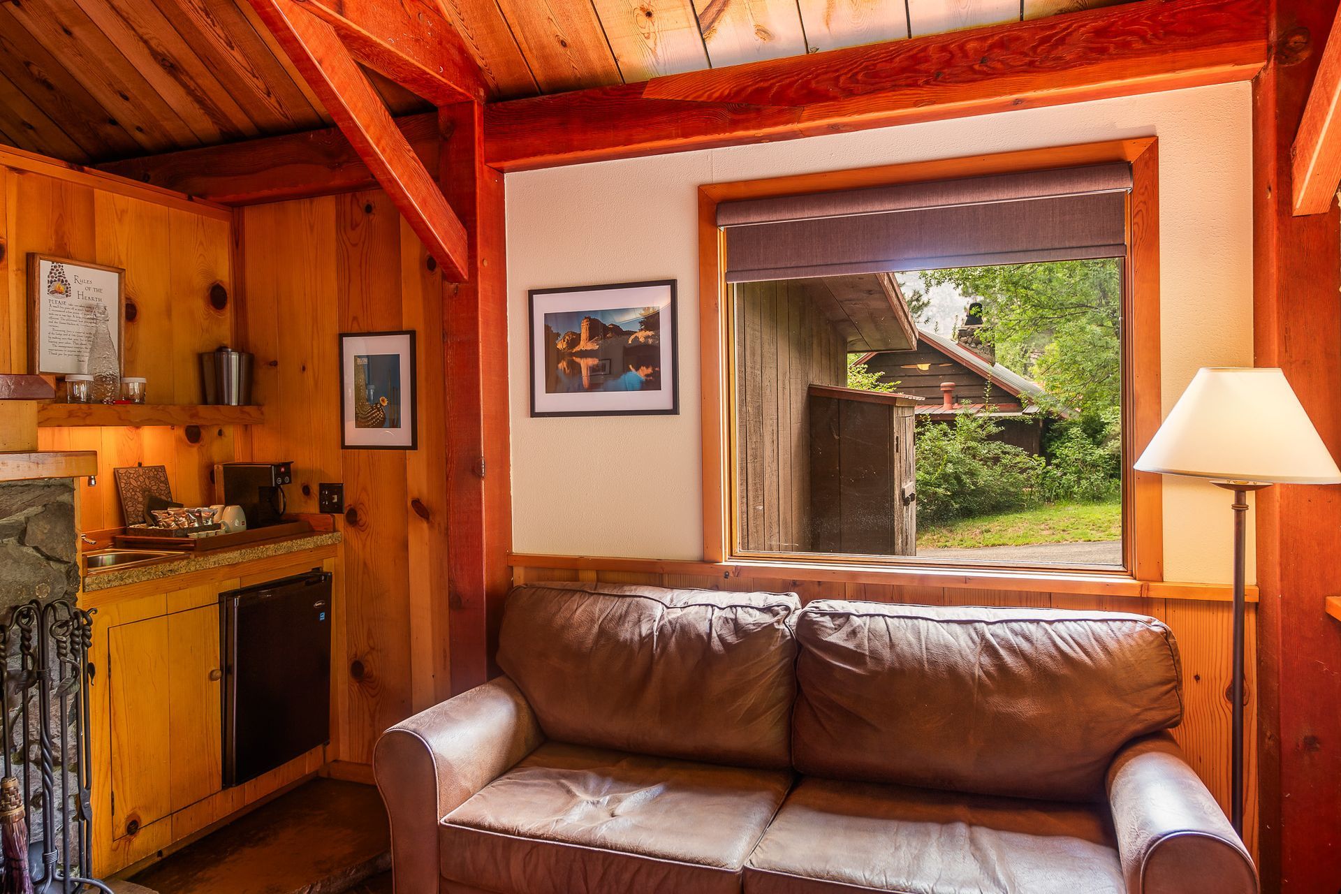 Cozy cabin interior with brown leather couch, window overlooking greenery, and wooden walls.