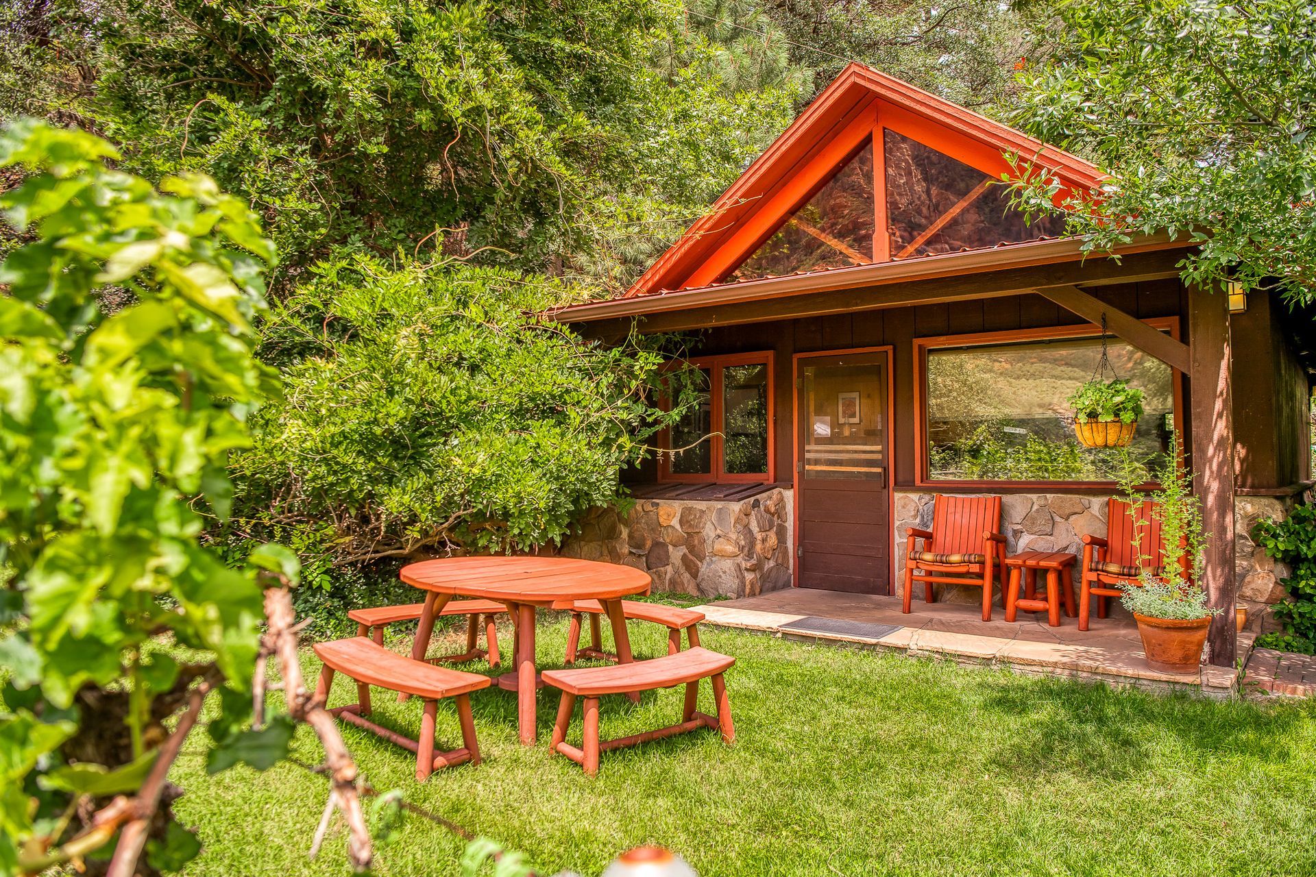 Wooden cabin with picnic table in a grassy yard surrounded by greenery.
