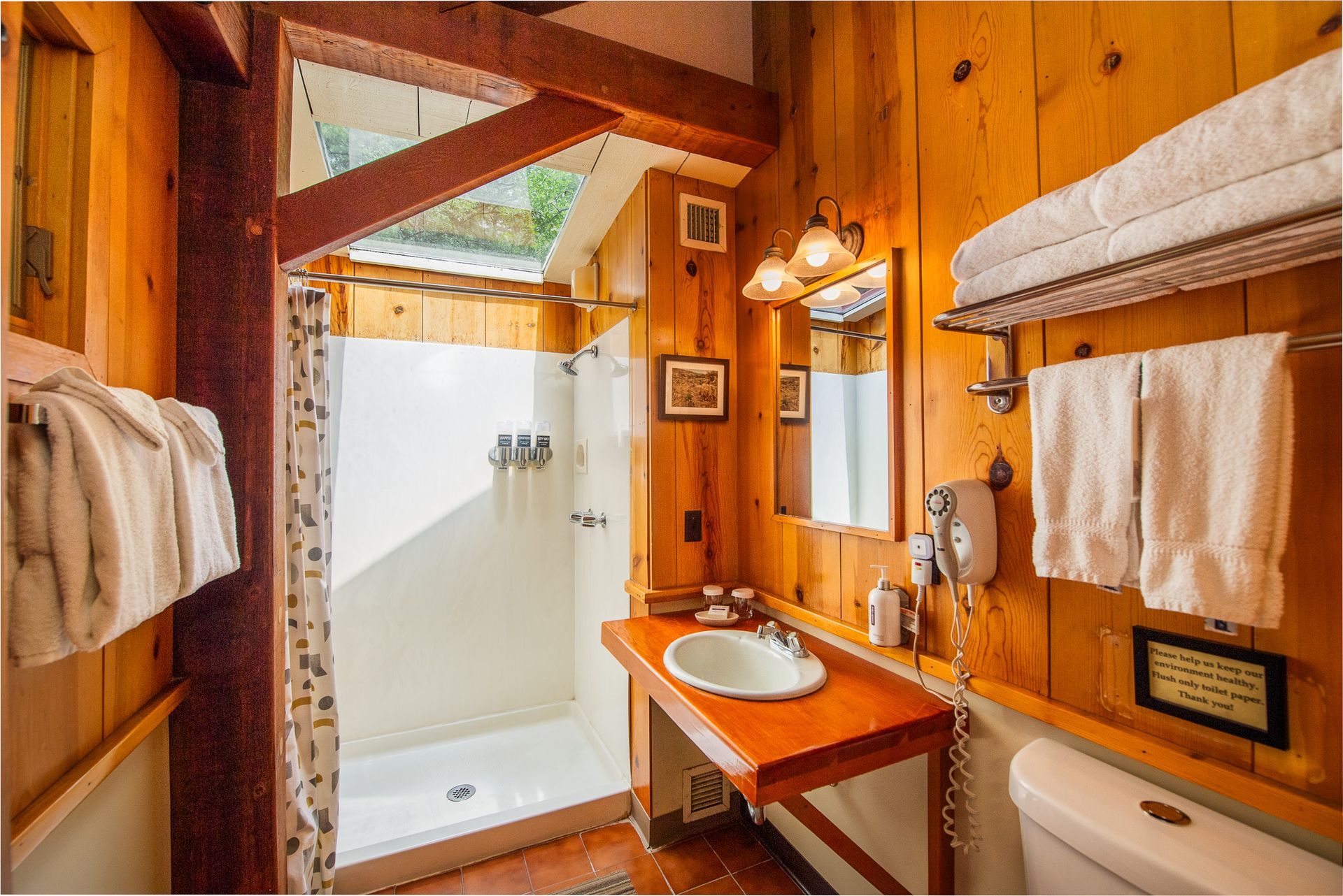 Bathroom with wood paneling, white shower, sink, and toilet. Towels and mirror are visible. Warm tones.