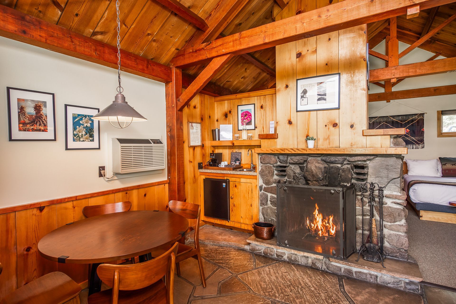 Cozy cabin interior with stone fireplace, wooden beams, and a dining area.