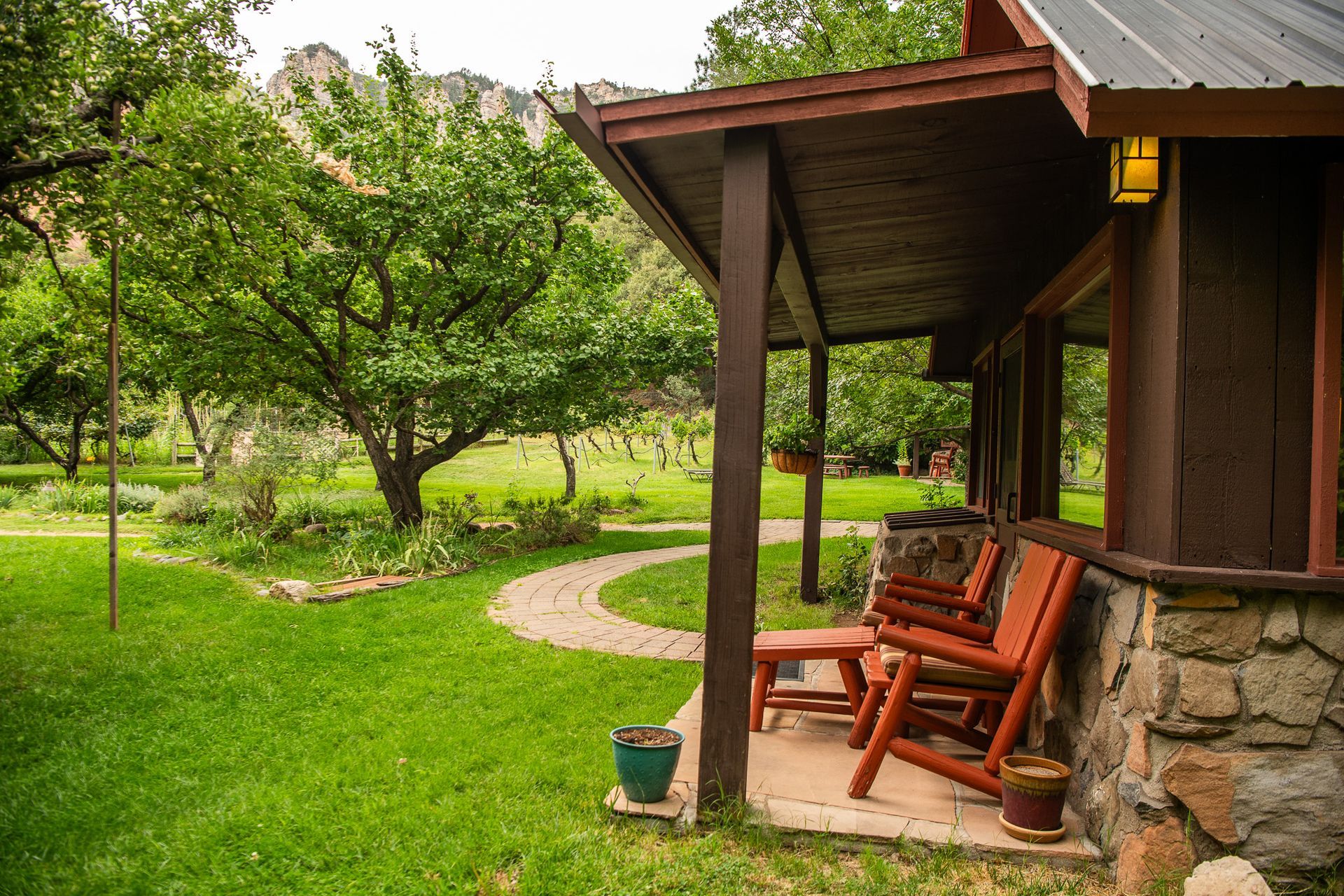 Porch with red chairs, stone wall, and lush green yard, trees and mountains in the background.
