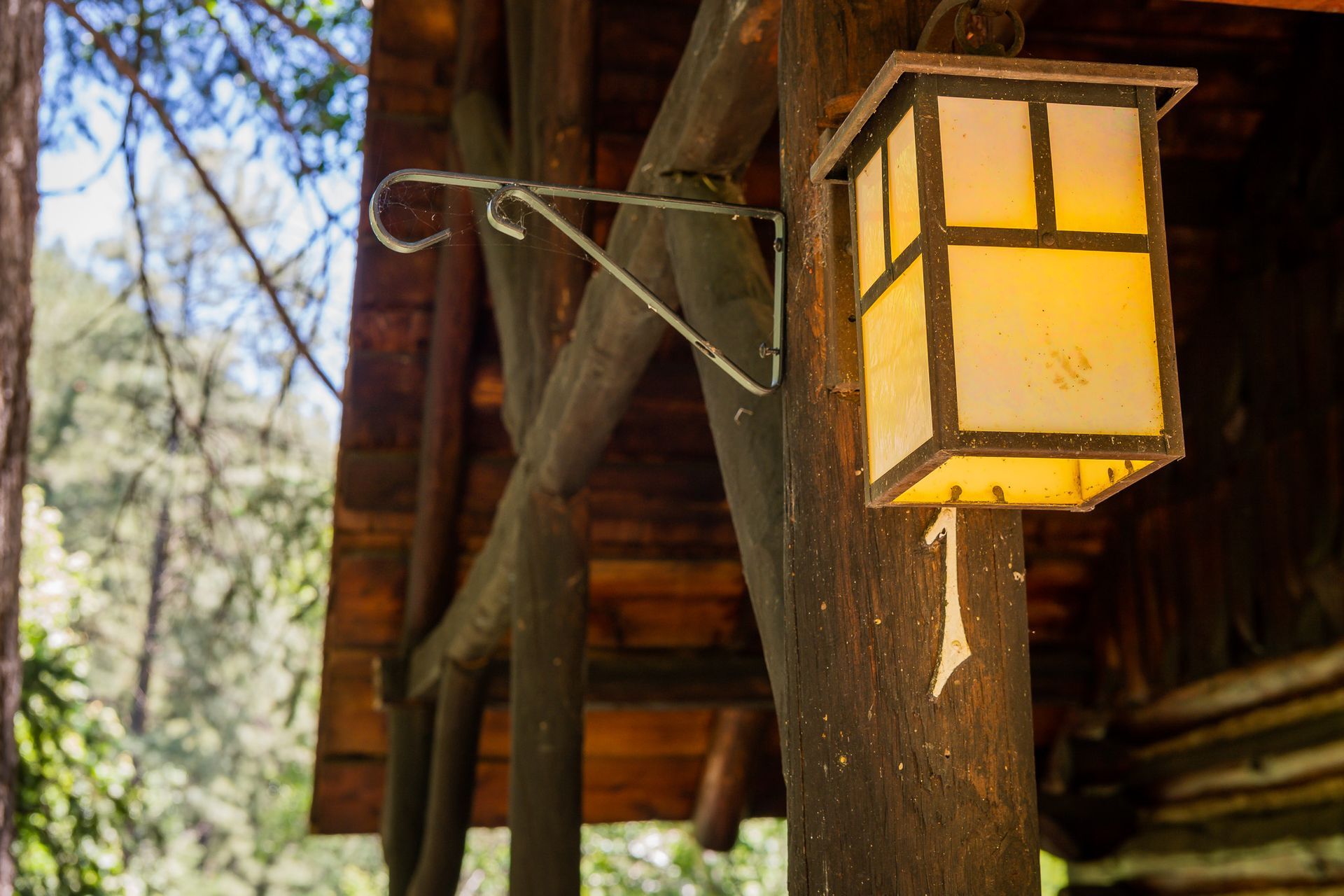 Lit lantern hanging on a wooden post, attached to a wooden cabin porch.