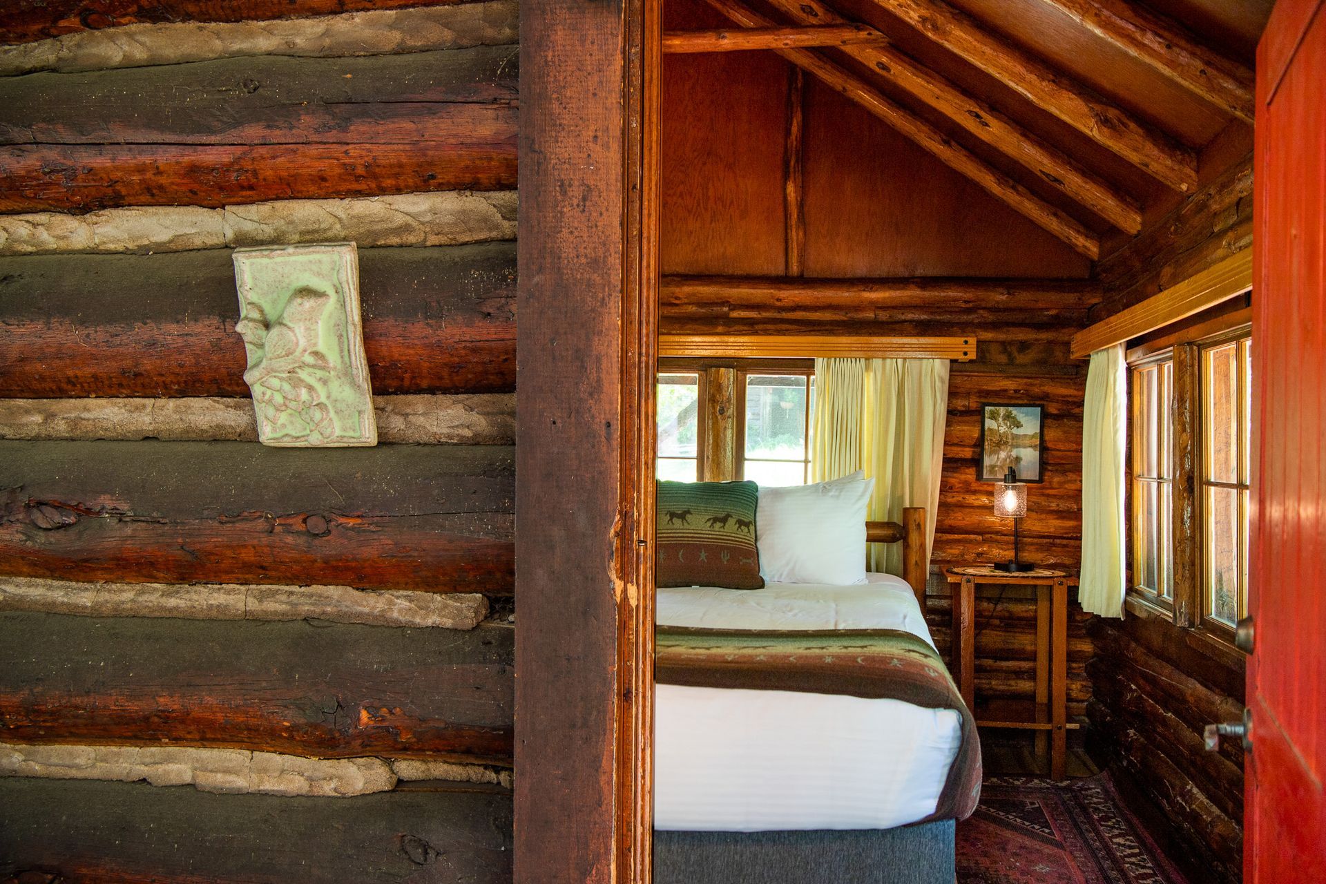 Log cabin interior: bed, small windows, exposed beams, rustic decor.