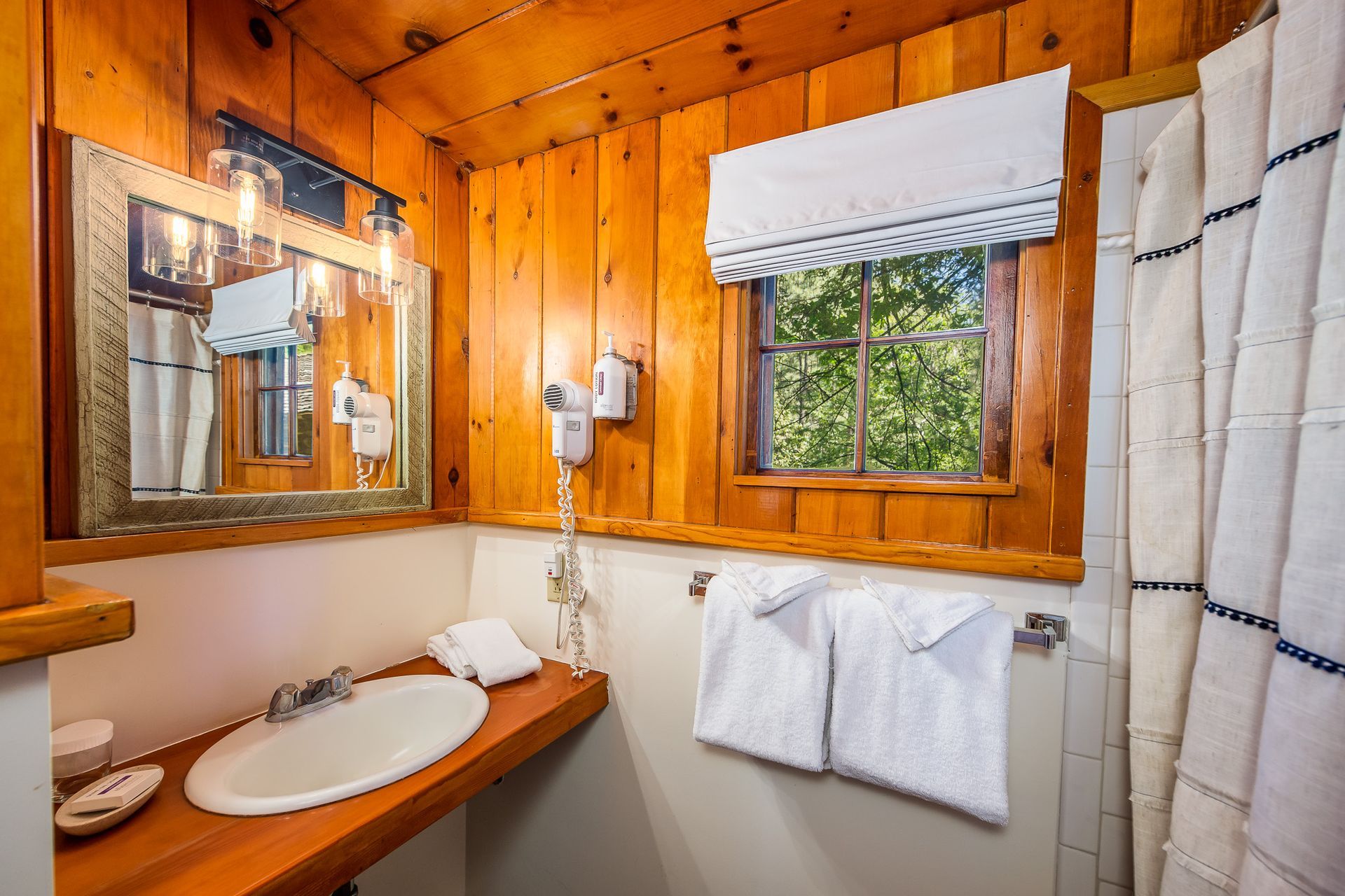 Bathroom with wooden walls, sink, towels, window with greenery, and shower curtain.