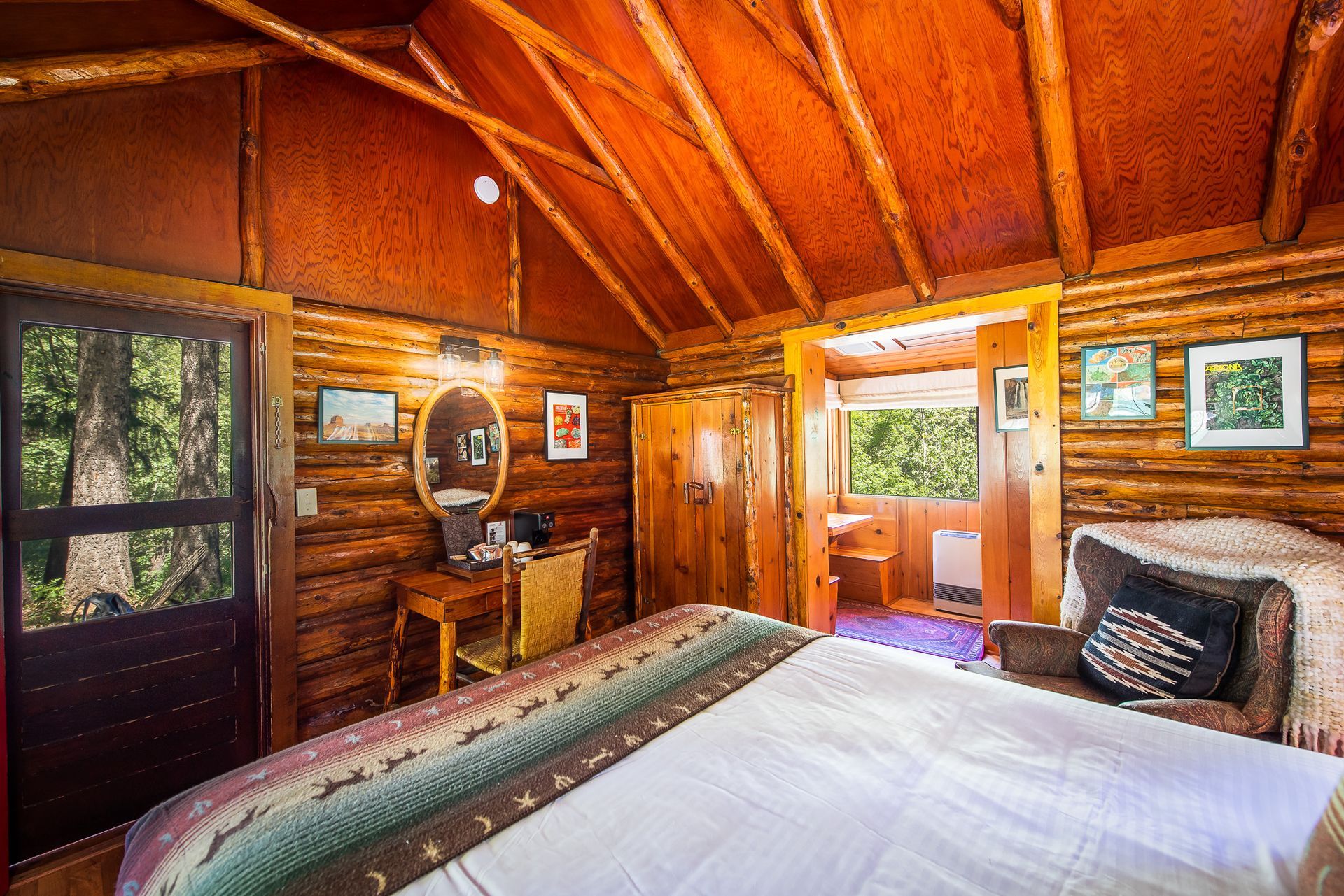 Cozy cabin bedroom with log walls, a bed, desk, and small outdoor balcony.