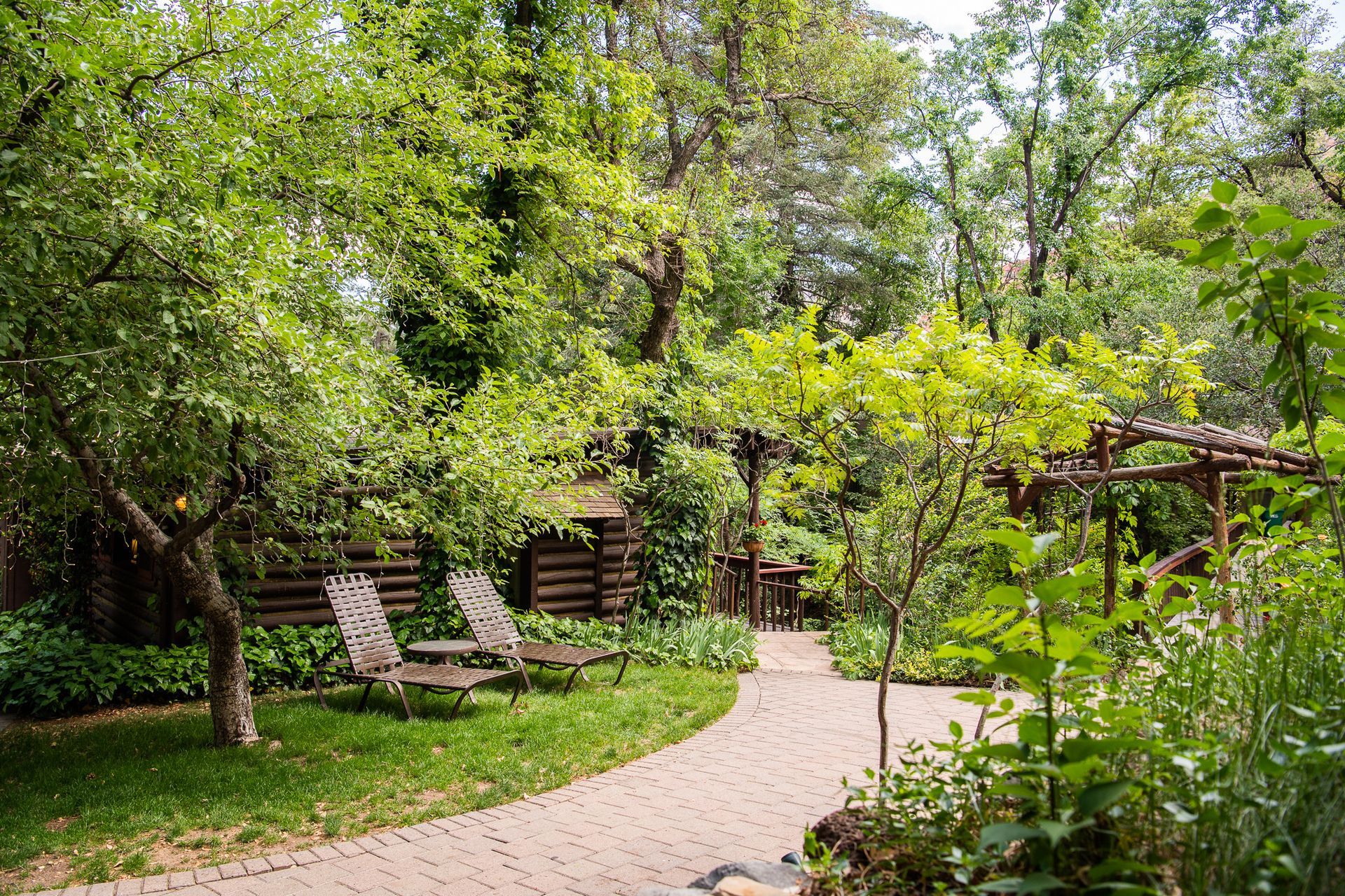 Path through a lush garden with trees, lounge chairs, and wooden structures.