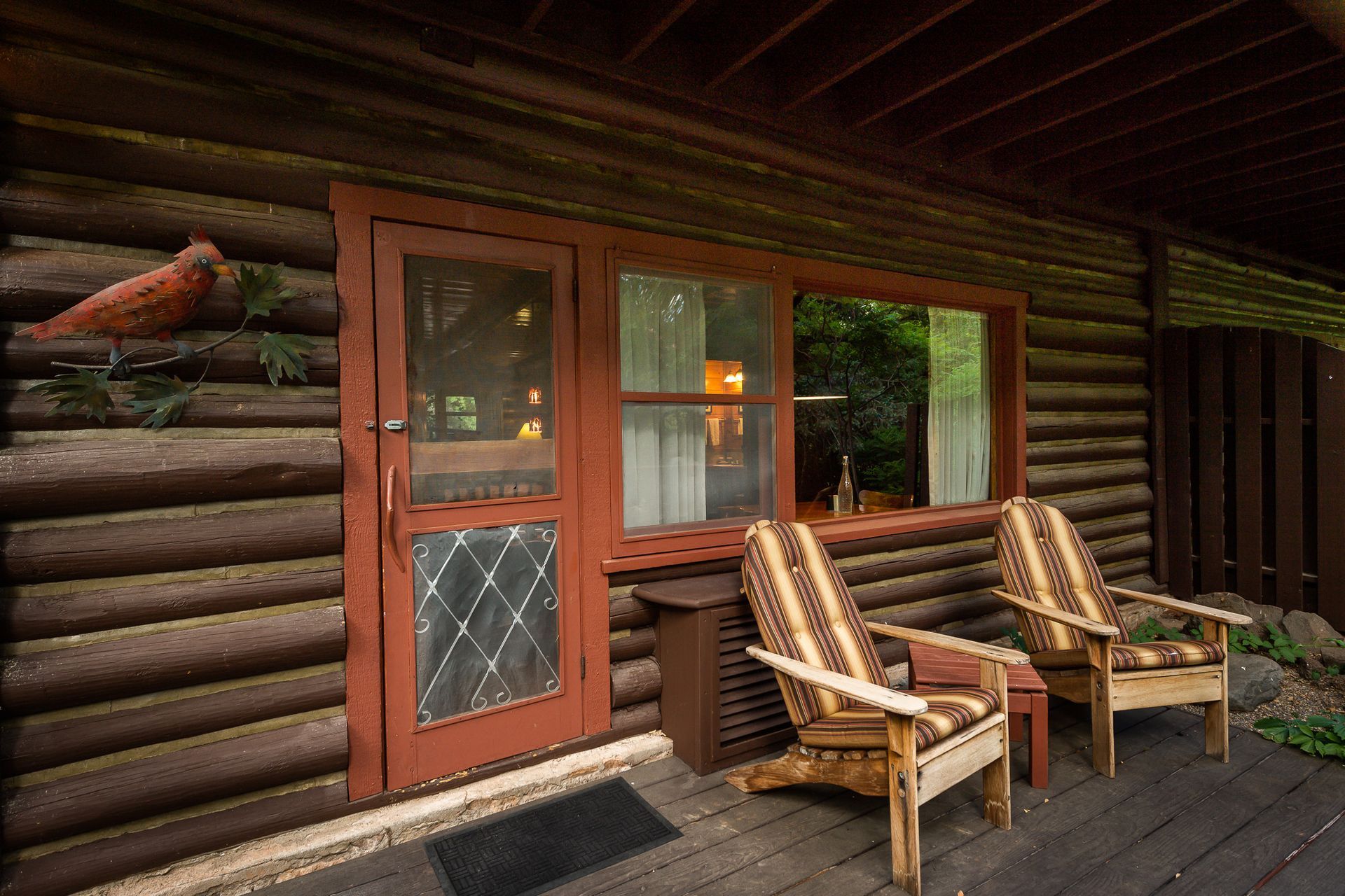 Log cabin porch with two wooden chairs, a red door, and a cardinal decoration.