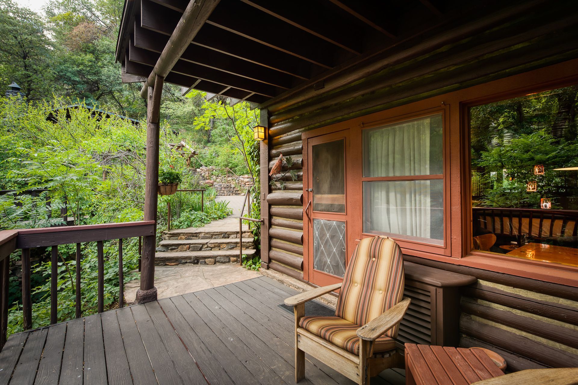 Rustic cabin porch with chair, lush greenery, steps.