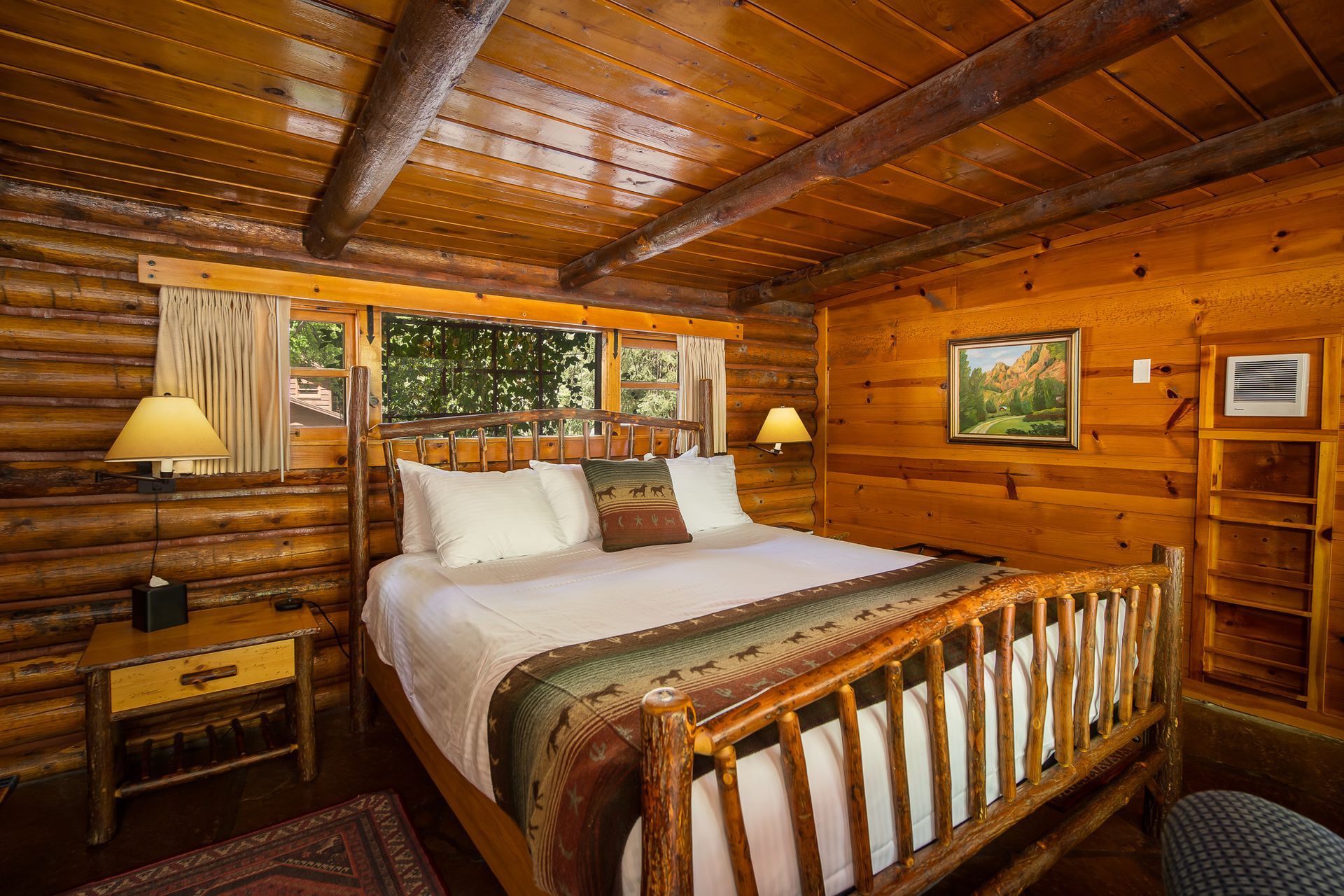 Rustic bedroom with a king-size bed, wood walls and ceiling, and a window overlooking trees.