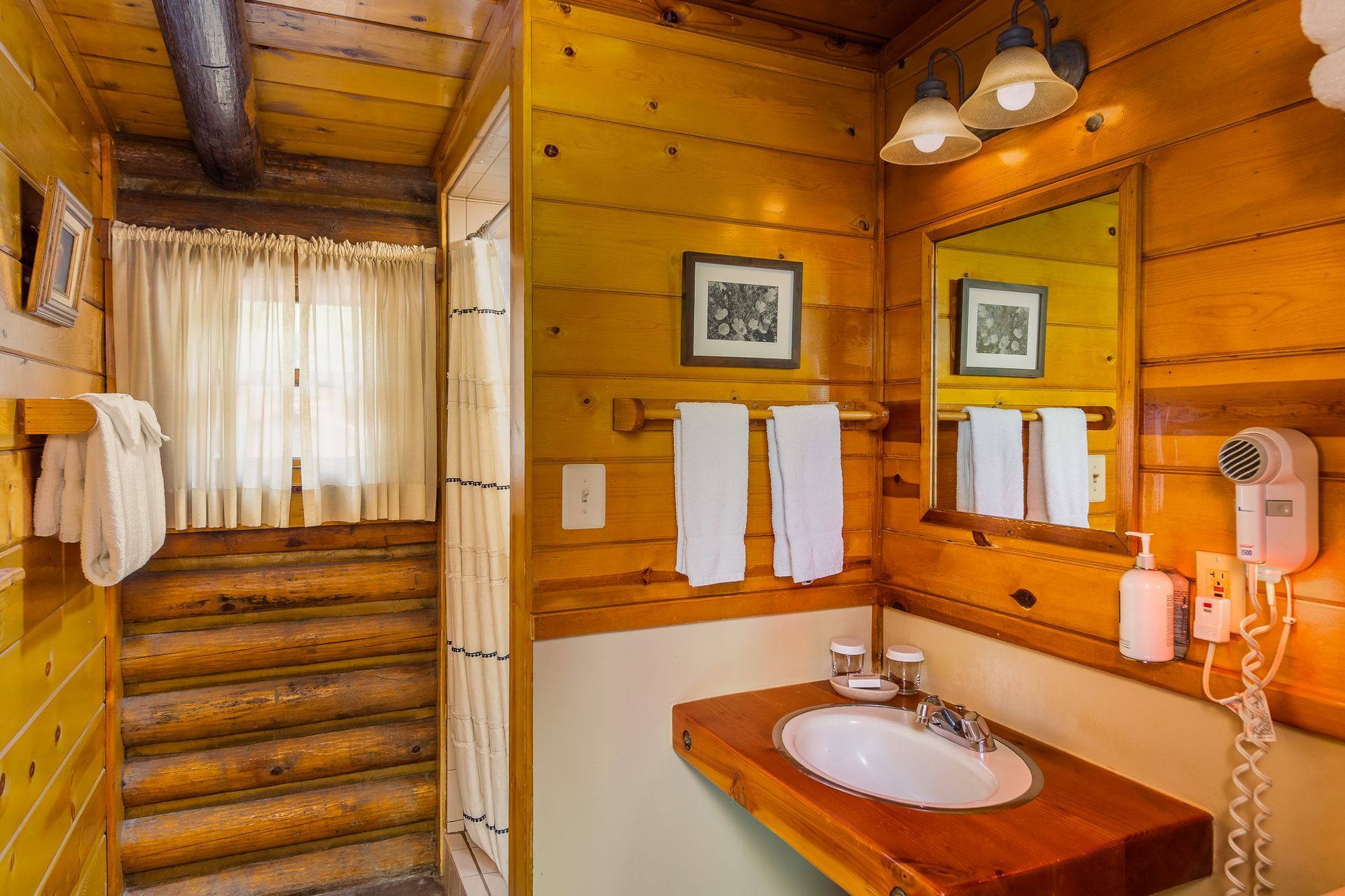Wooden cabin bathroom with sink, mirror, towels, and shower entrance with curtain.