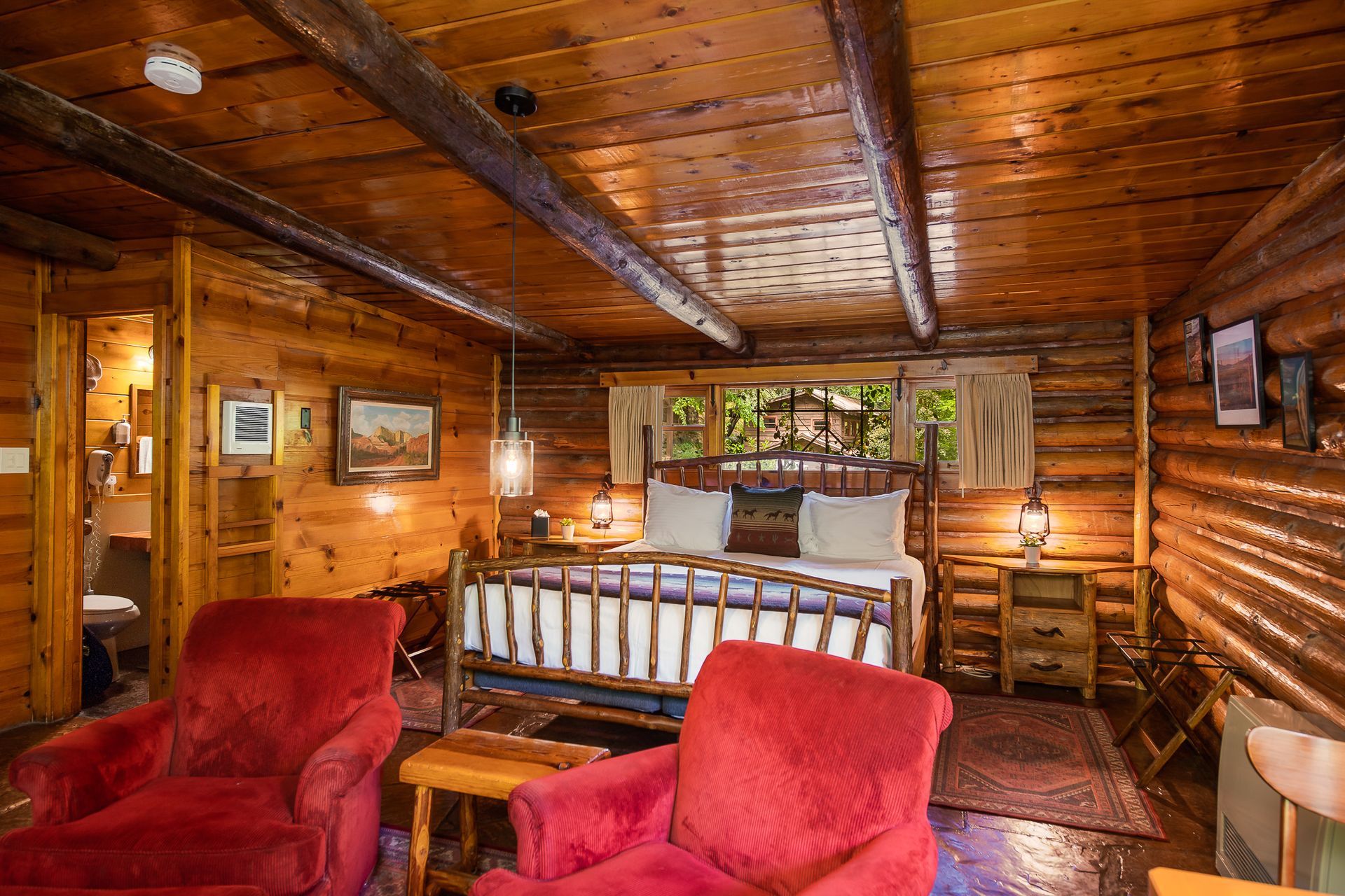 Cozy rustic cabin bedroom with red armchairs, wooden bed, and log walls.