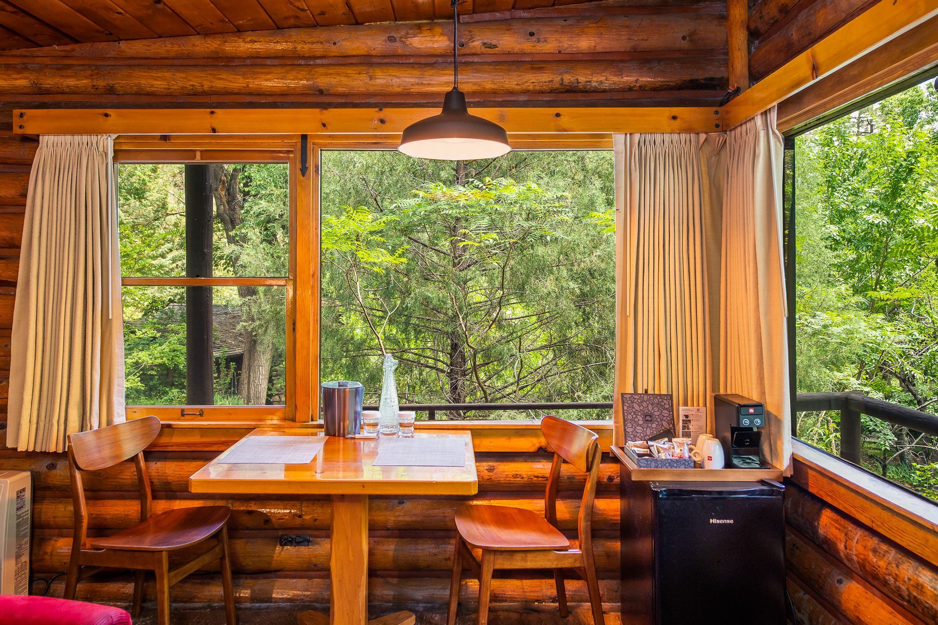 Cozy cabin interior with a table, chairs, and window overlooking a green forest.