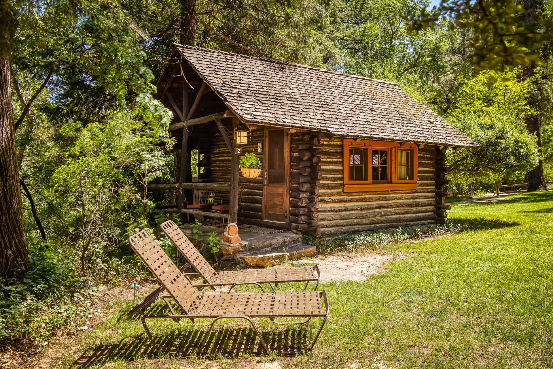 Cozy log cabin with a covered porch, two lounge chairs on the grass.
