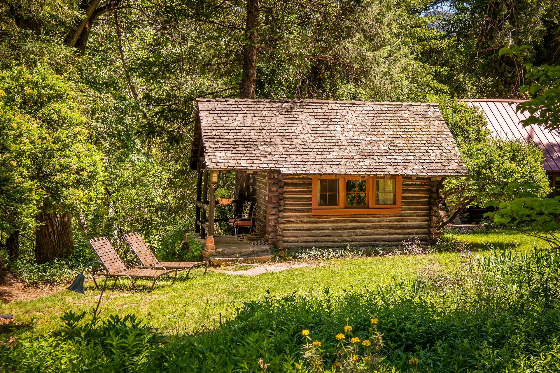 Cabin made of logs sits in a grassy area. Two lounge chairs are near the cabin.
