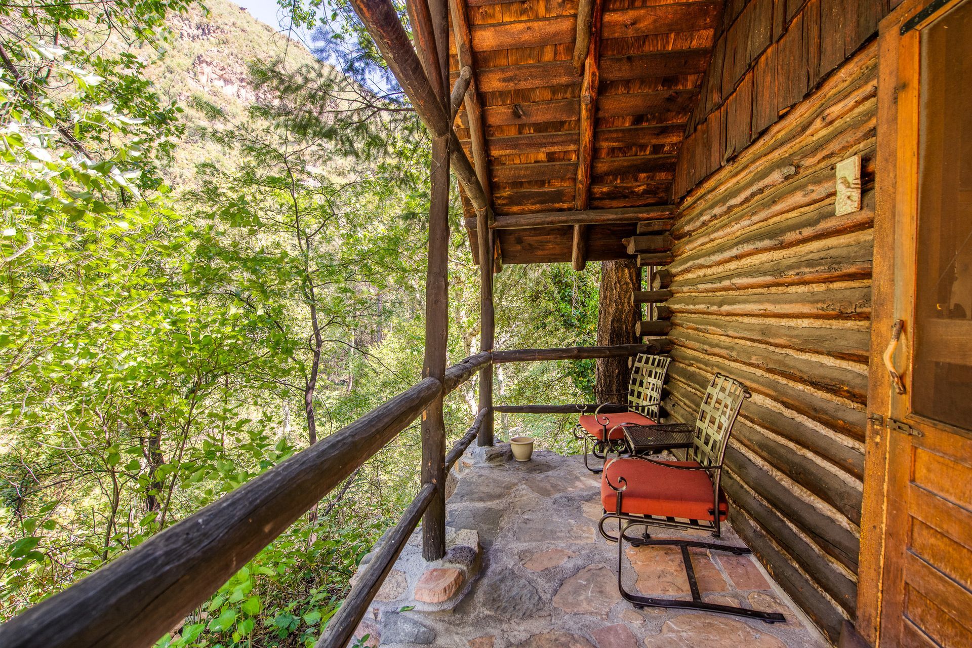Wooden porch with stone floor overlooking lush green foliage.