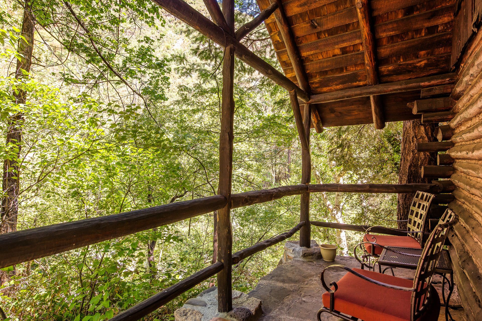 Rustic porch with red chairs, overlooking a green forest.